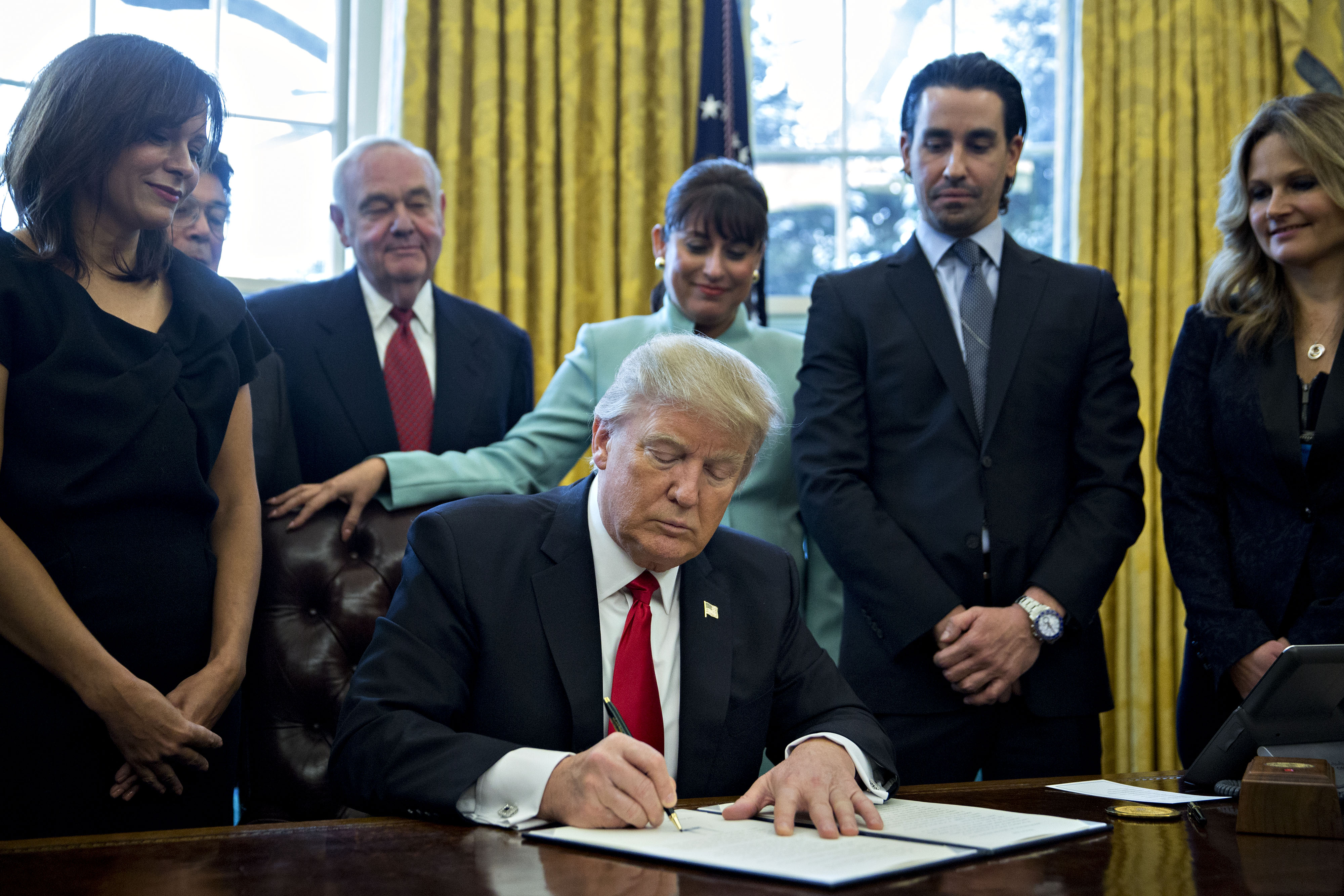 U.S. President Donald Trump signs an executive order surrounded by small business leaders in the Oval Office of the White House in in Washington, D.C., U.S., on Monday, Jan. 30, 2017.