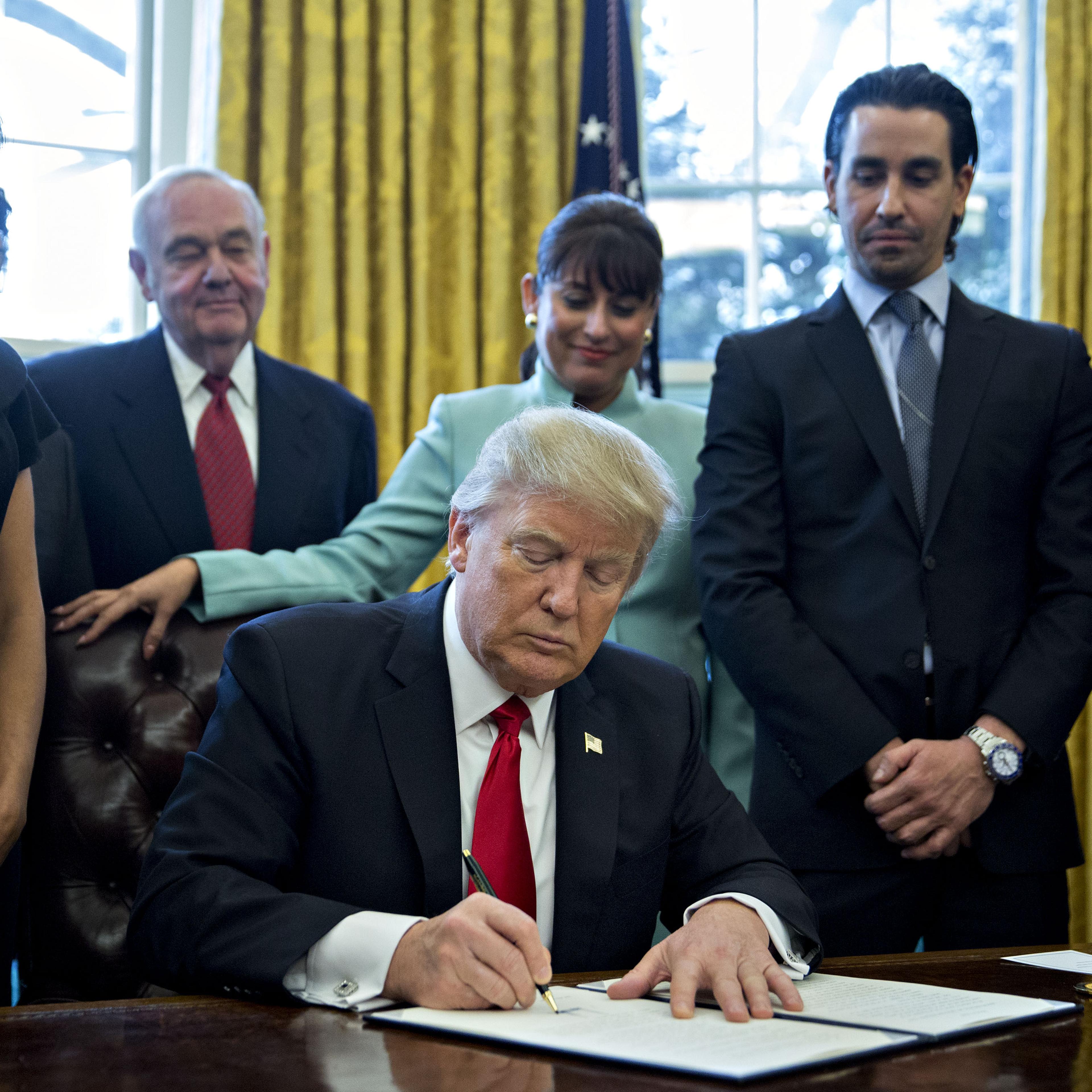 U.S. President Donald Trump signs an executive order surrounded by small business leaders in the Oval Office of the White House in in Washington, D.C., U.S., on Monday, Jan. 30, 2017.