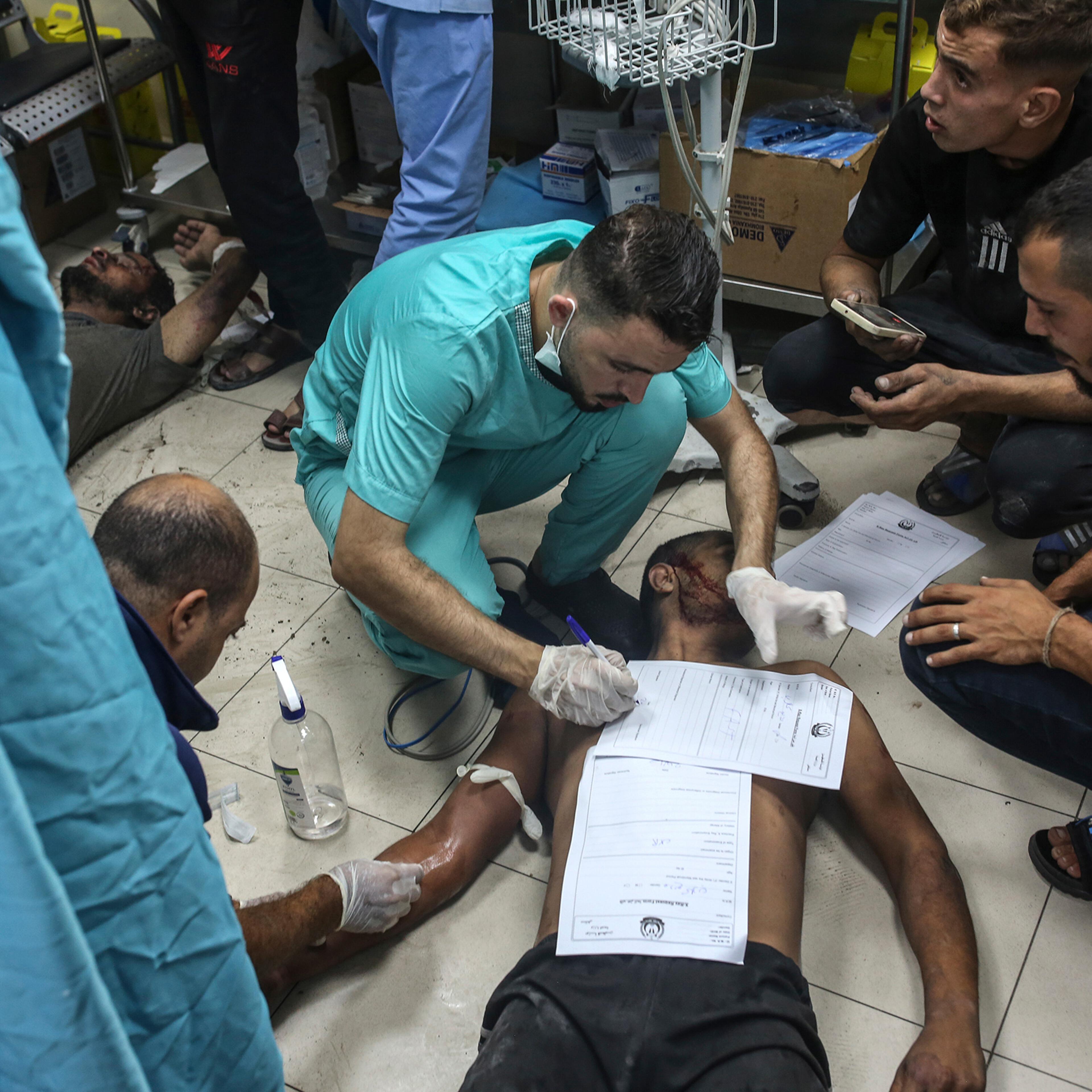 A doctor fills out paperwork on top of a patient on the floor at Nasser Medical Hospital in Khan Younis, in the southern Gaza Strip, on Oct. 24.