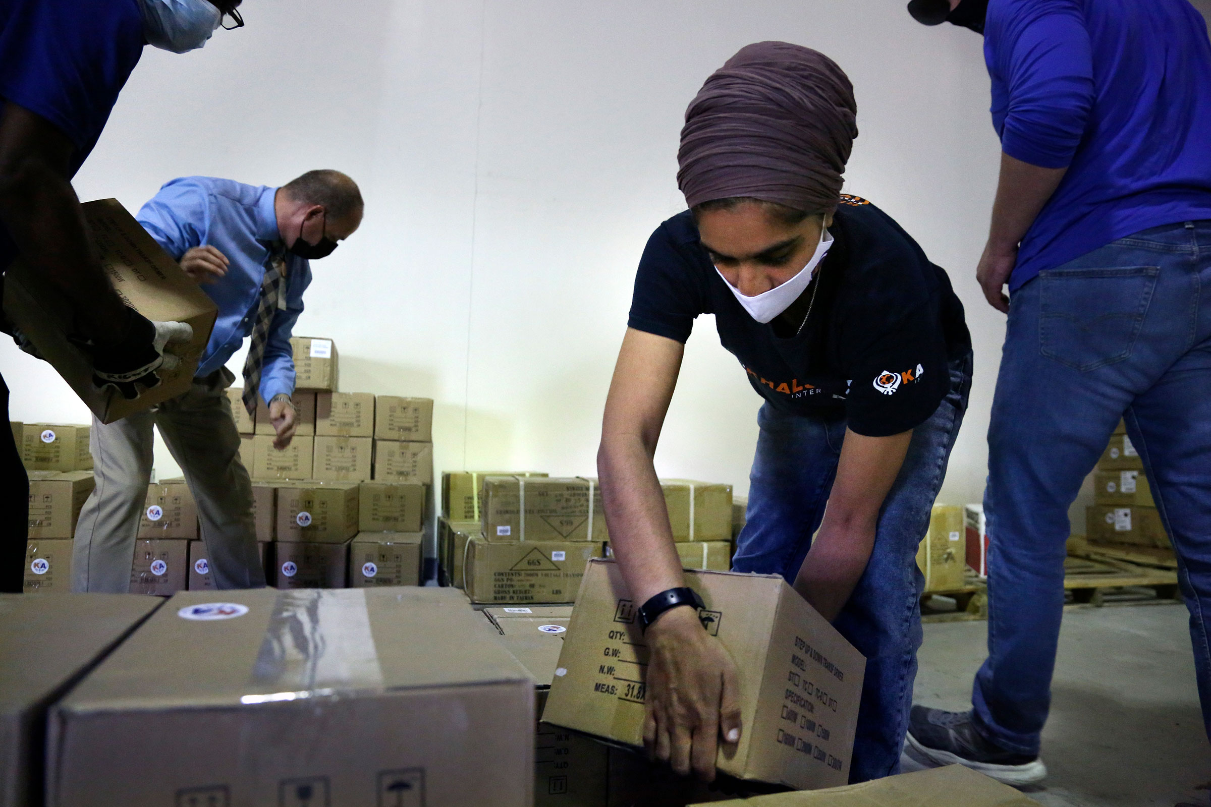 Tim Williams, warehouse assistant for Medisys, Ray Fredericks, assistant director for Medisys, Dr. Abhu Kaur with Khalsa Aid, and Michael Stack, healthcare account representative for Grainger, load dozens of electrical transformers onto a pallet to be sh