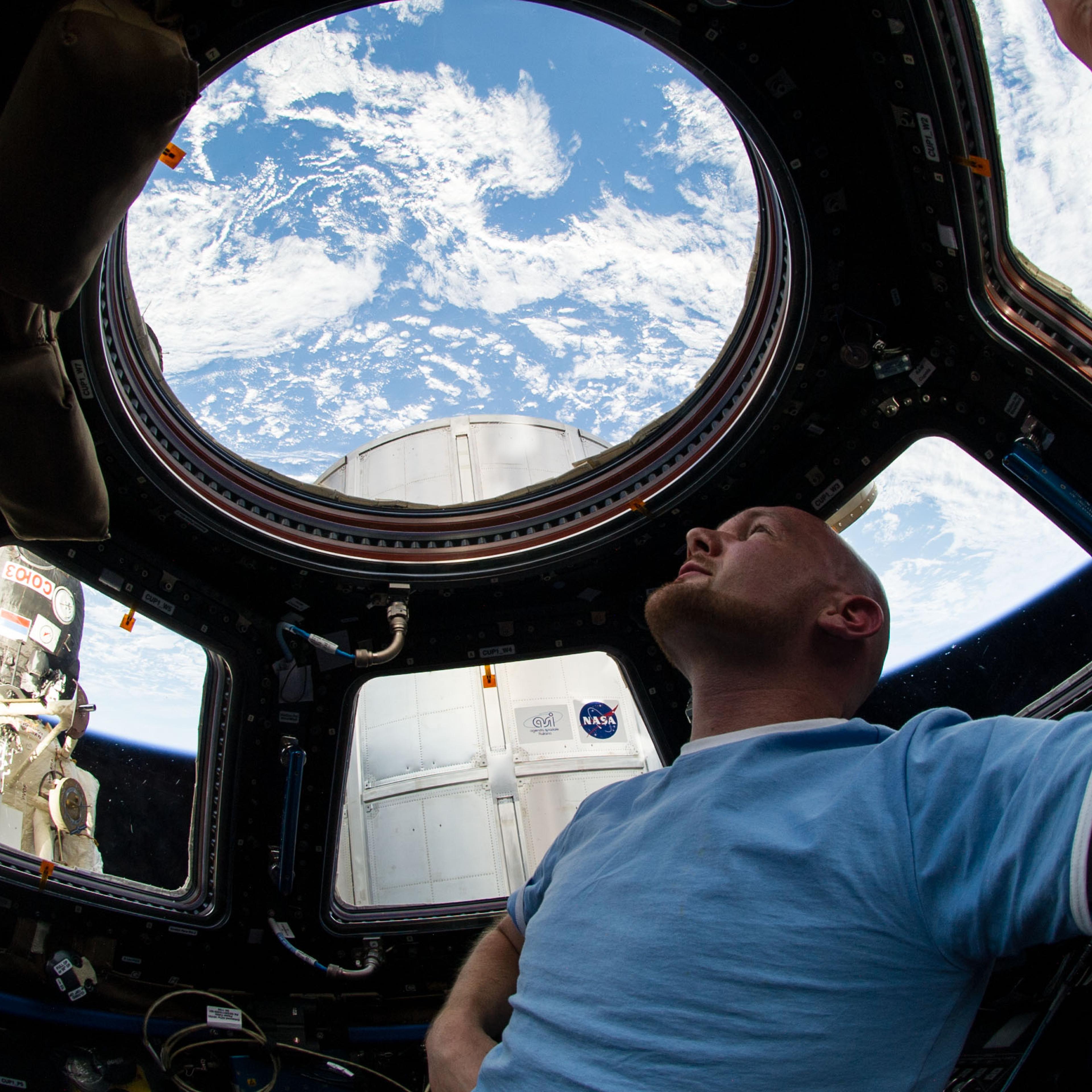 Astronaut Alexander Gerst enjoys the view of Earth from the windows in the Cupola of the International Space Station. A blue and white part of Earth is visible through the windows.