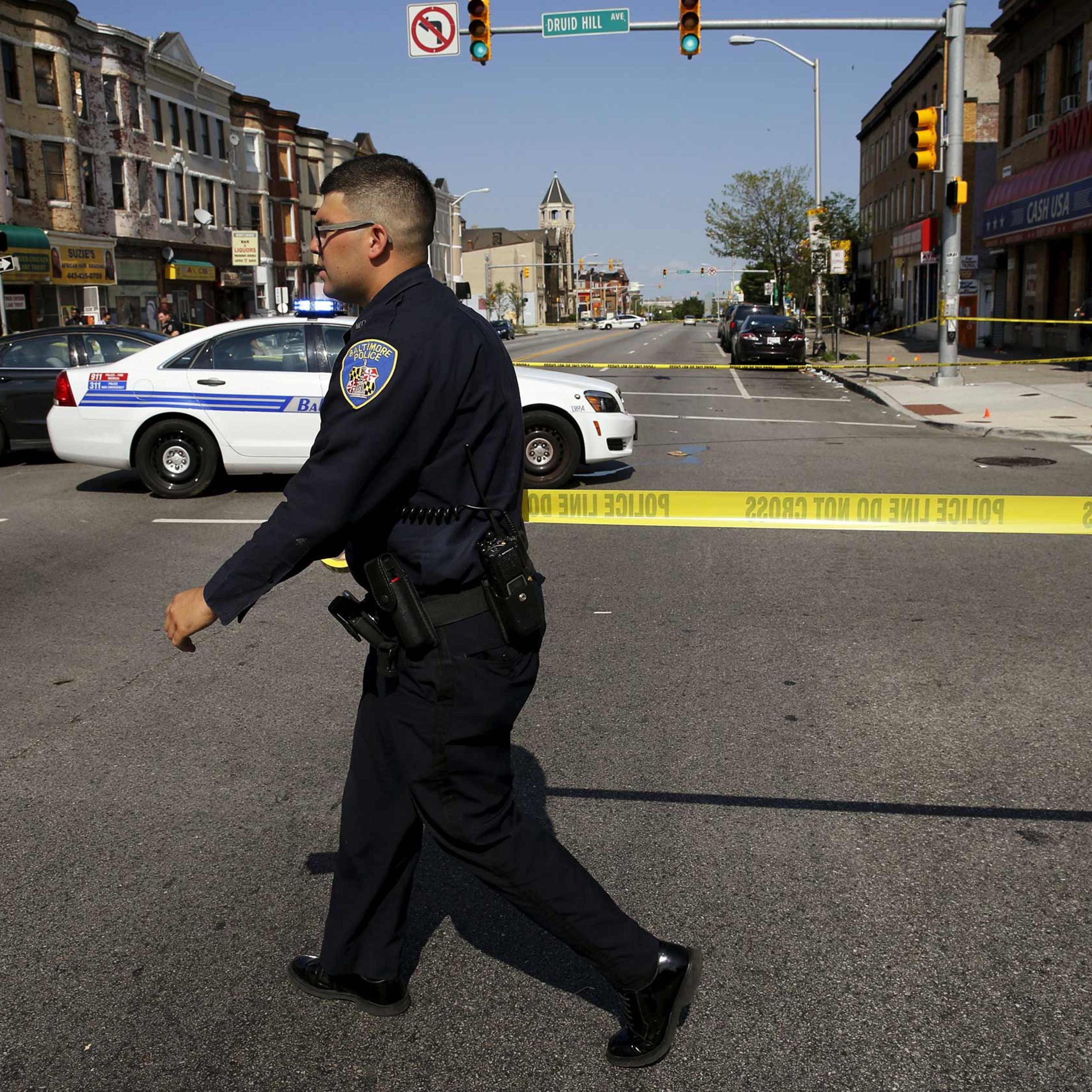 Baltimore police officer attempts to secure a crime scene with tape at the scene of a shooting in West Baltimore