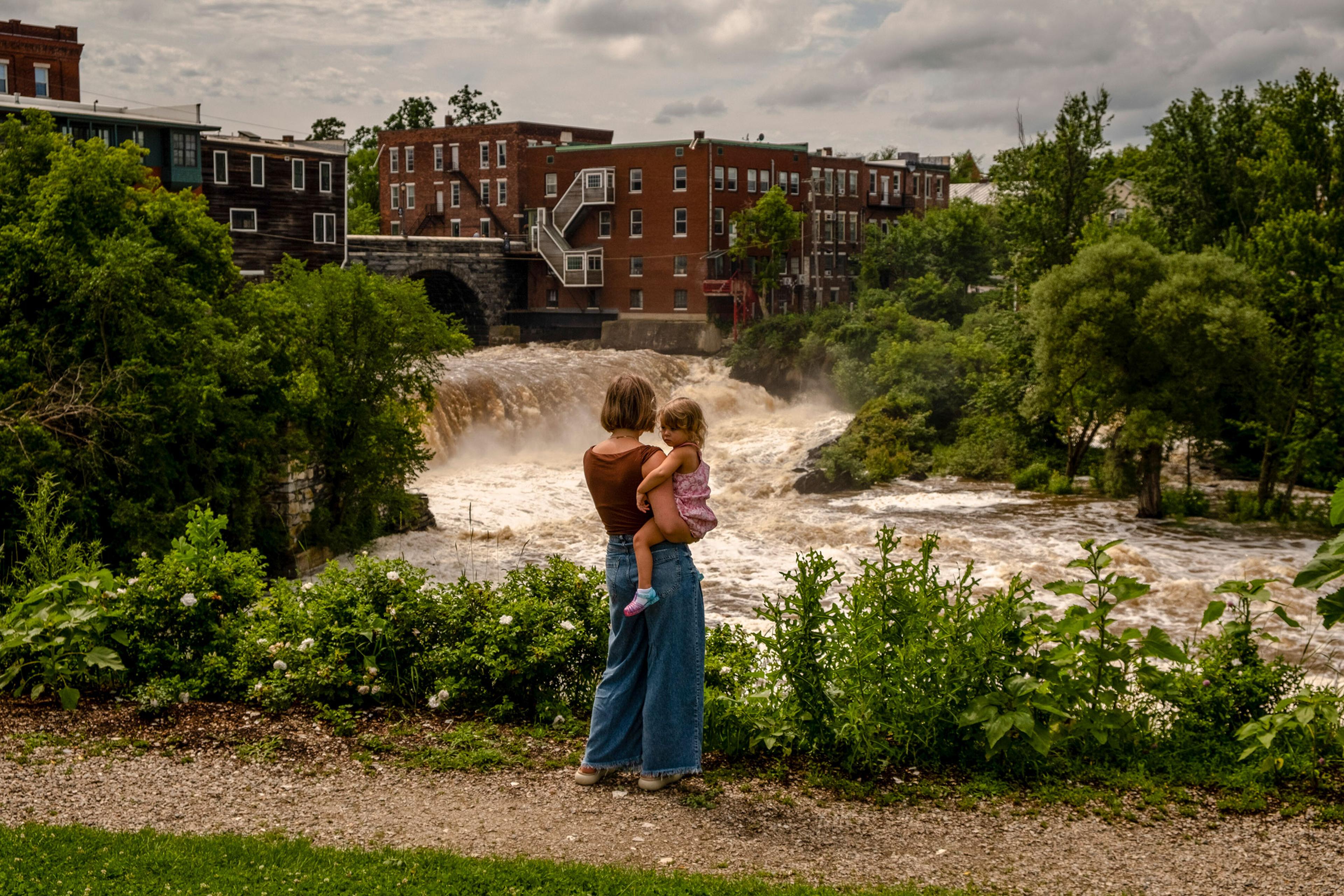 Lauren Rowley and her daughter Ursula, 2, look at the surging Otter Creek River in downtown Middlebury, Vt., on July 14, 2023. Vermont began new flood protection efforts after being battered by Tropical Storm Irene in 2011. Many appeared to be effective,