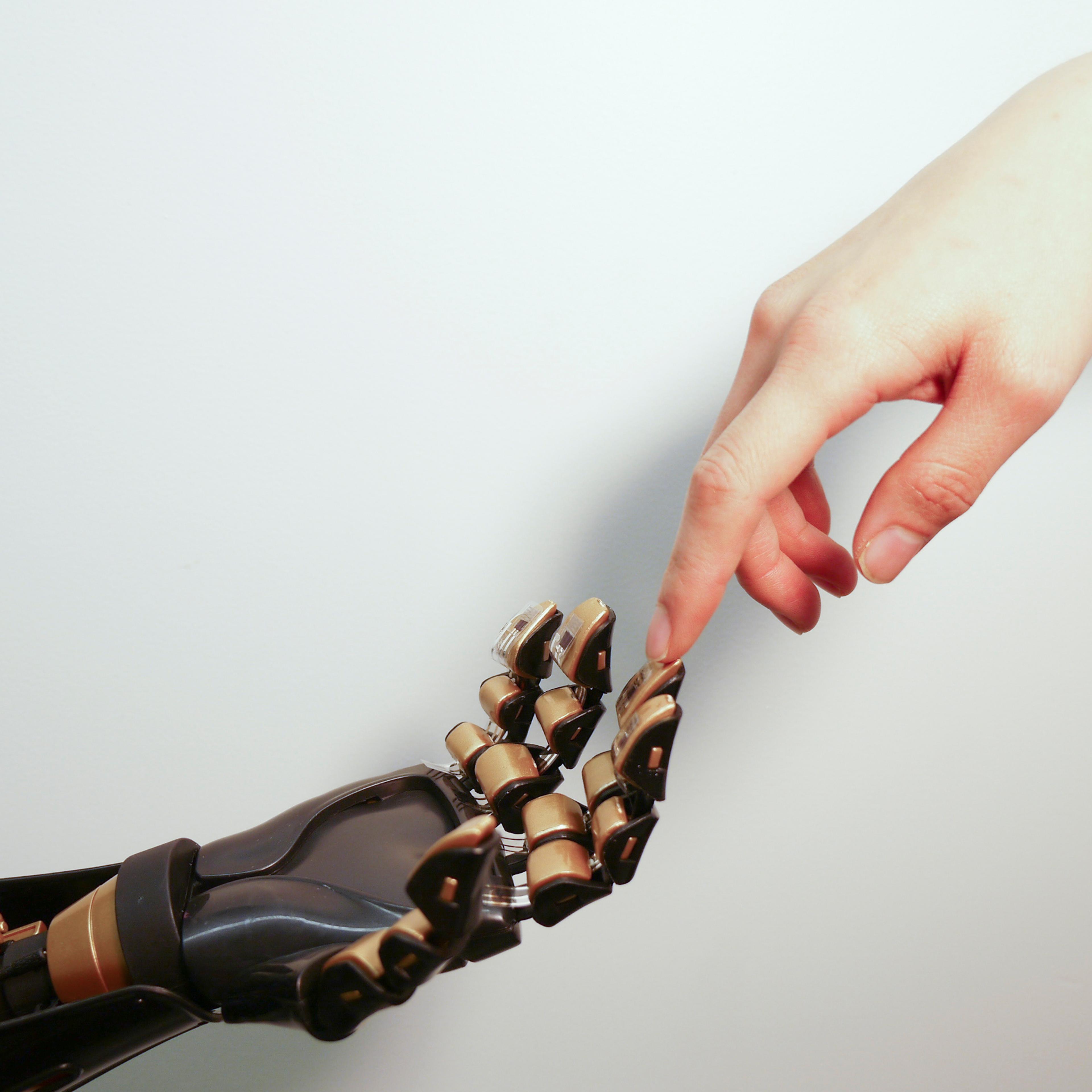 Human finger touches robotic finger. The transparent plastic and black device on the golden “fingertip” is the skin-like sensor developed by Stanford engineers. This sensor can detect pressure and transmit that touch sensation to a nerve cell. The goal i