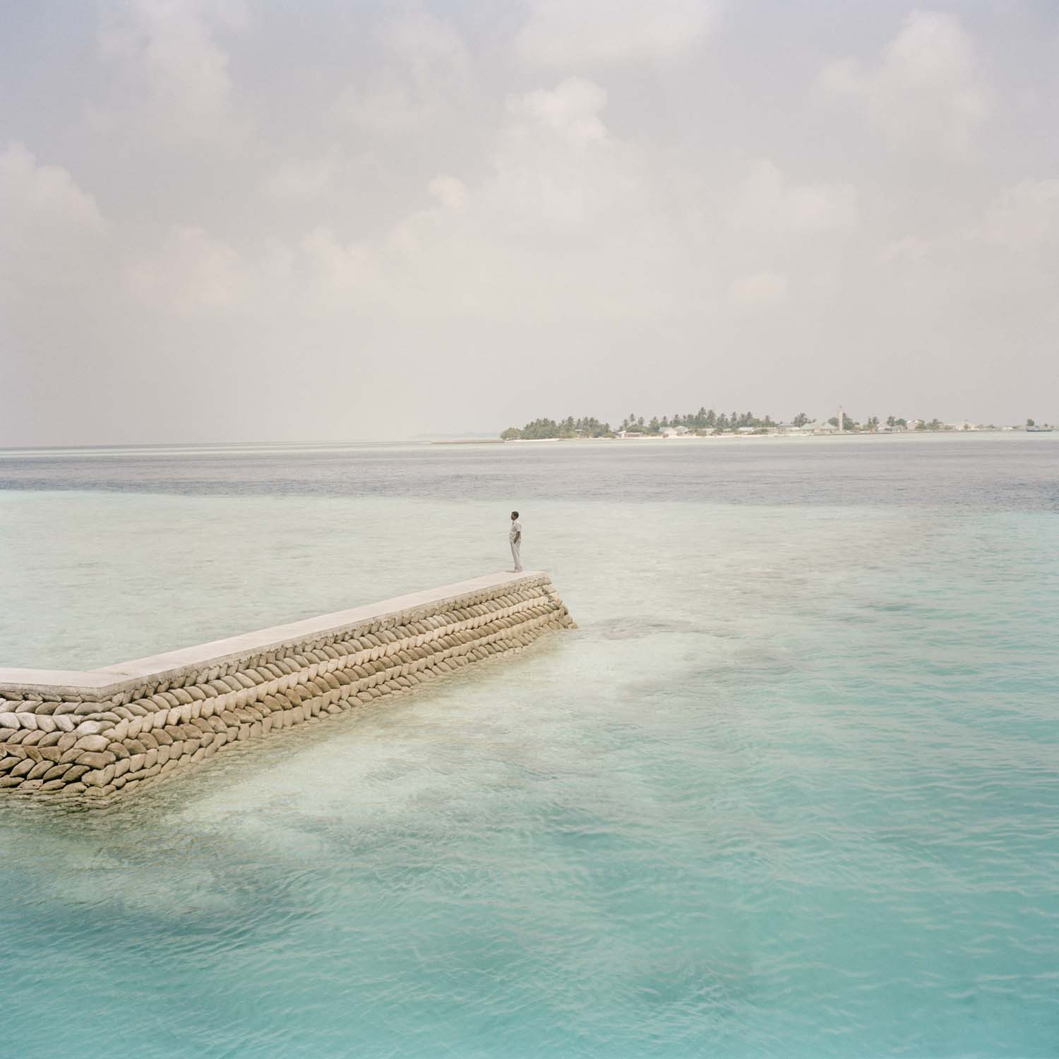 A man stands at the end of a seawall on Dhiggaru island, Meemu atoll. March 2009.