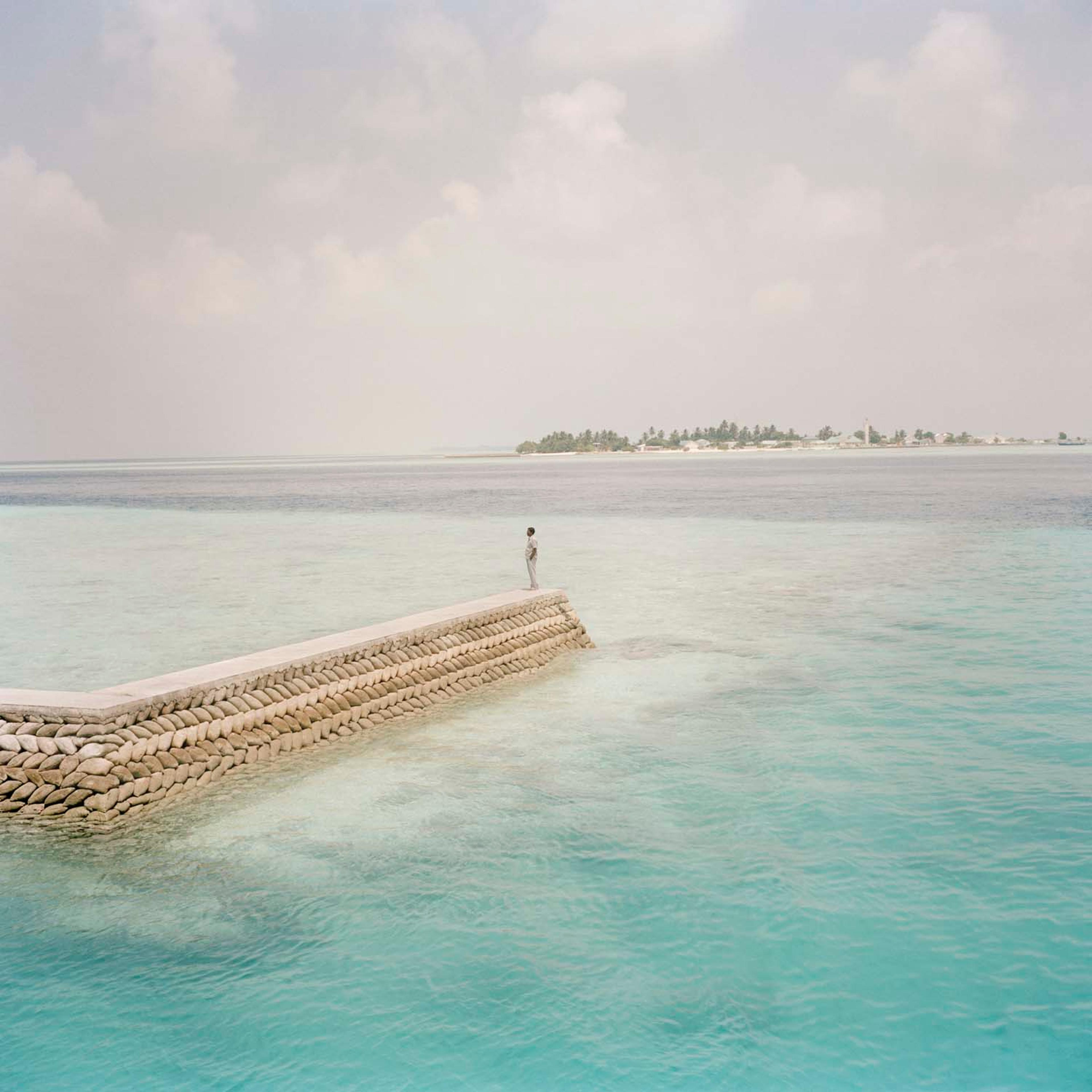 A man stands at the end of a seawall on Dhiggaru island, Meemu atoll. March 2009.