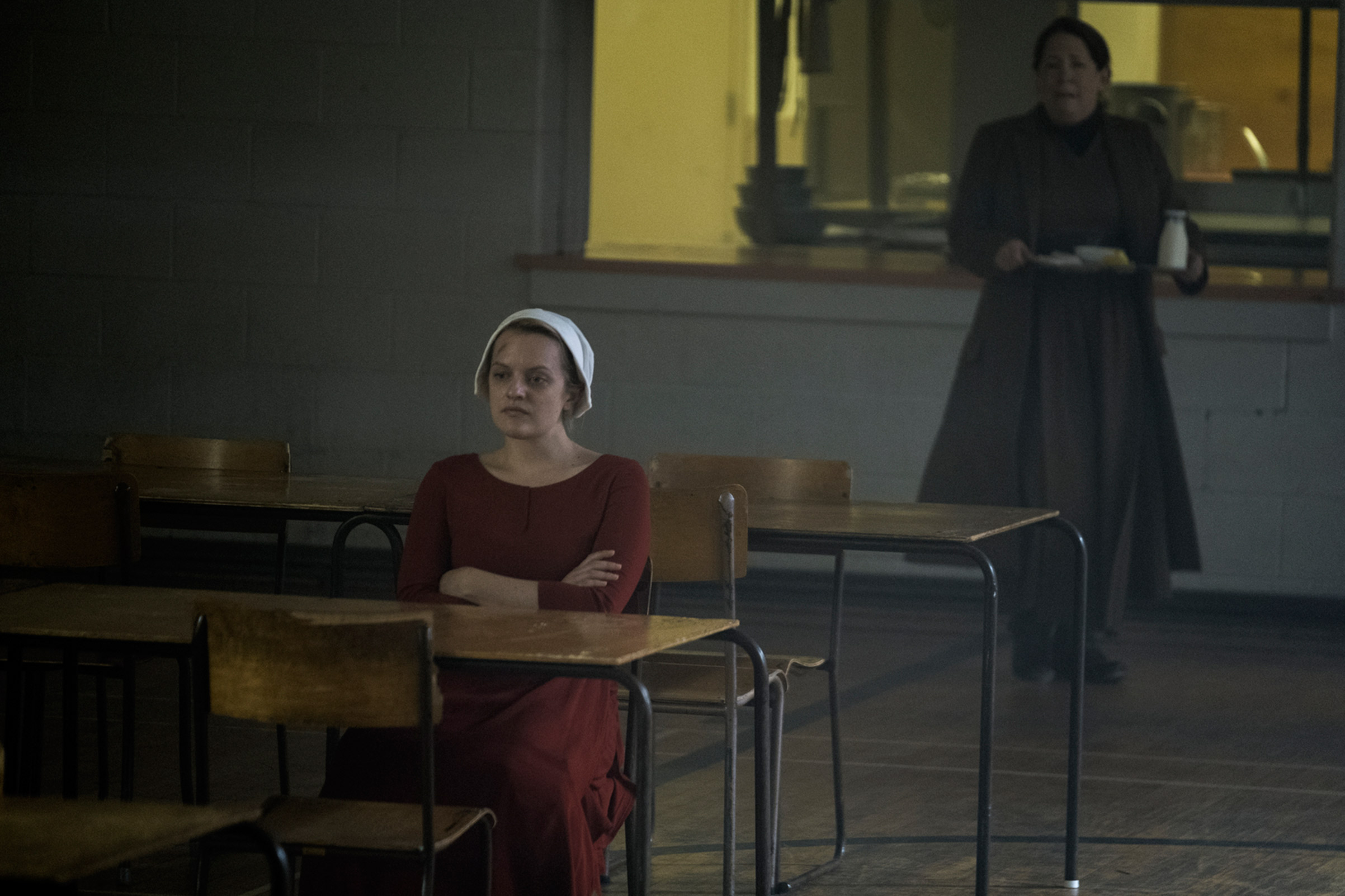 The Handmaid Offred (Elisabeth Moss), who is with child, refusing to eat, per orders from the Handmaids' instructor Aunt Lydia (Ann Dowd), pictured in the back. 