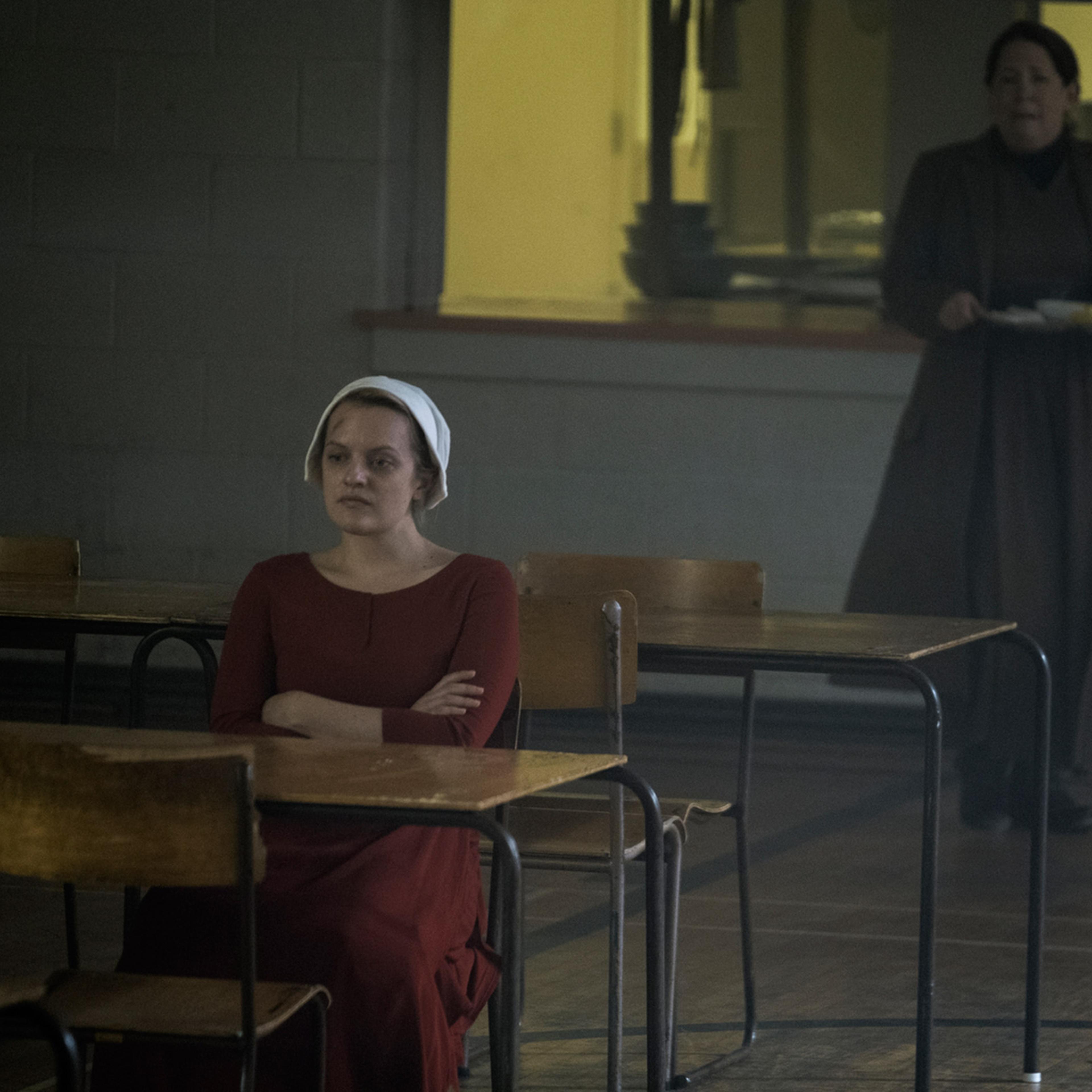 The Handmaid Offred (Elisabeth Moss), who is with child, refusing to eat, per orders from the Handmaids' instructor Aunt Lydia (Ann Dowd), pictured in the back.