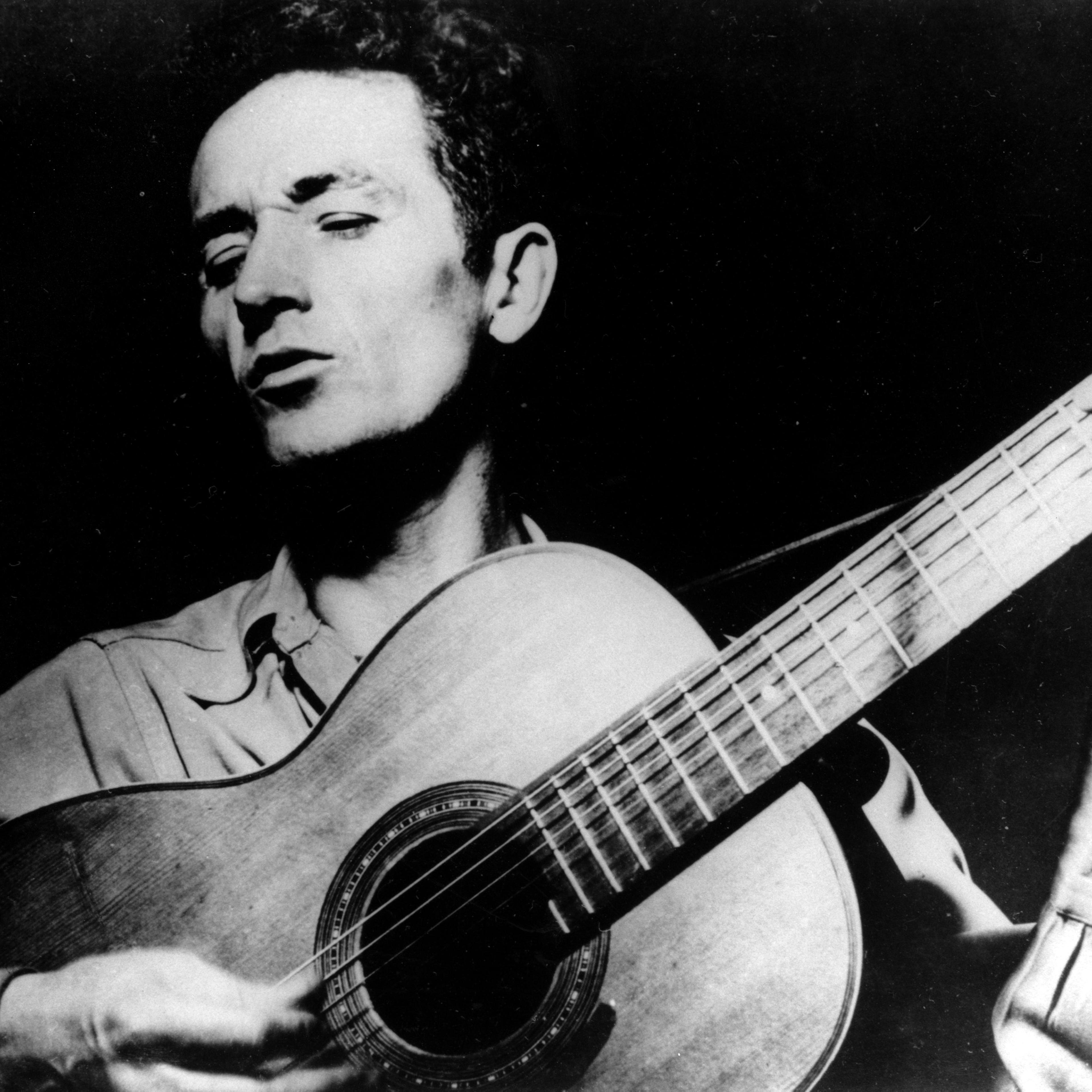 Folk singer, Woody Guthrie, singing a song and playing his guitar.