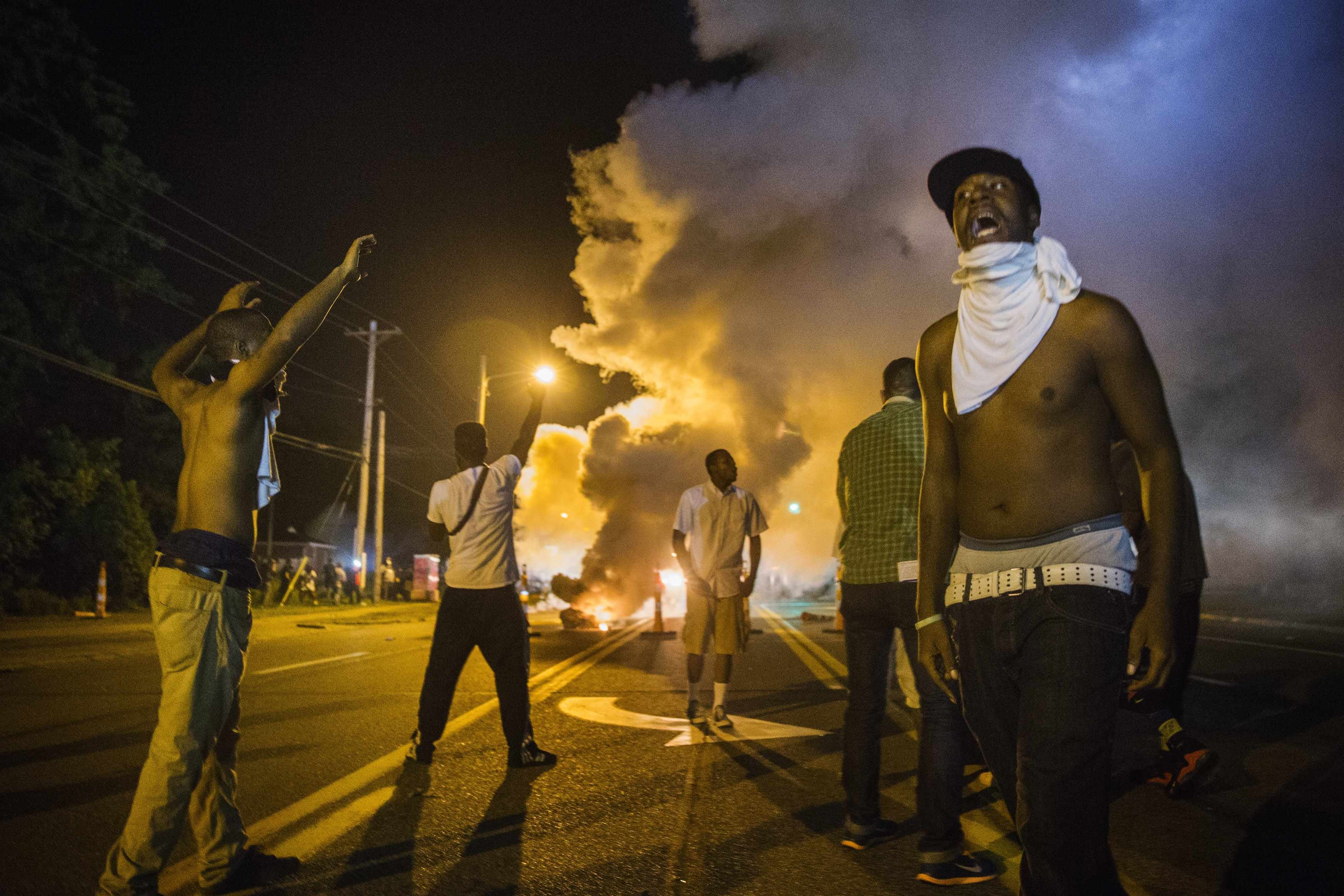 Demonstrators stand in the middle of West Florissant as they react to tear gas fired by police during ongoing protests in reaction to the shooting of Brown, near Ferguson
