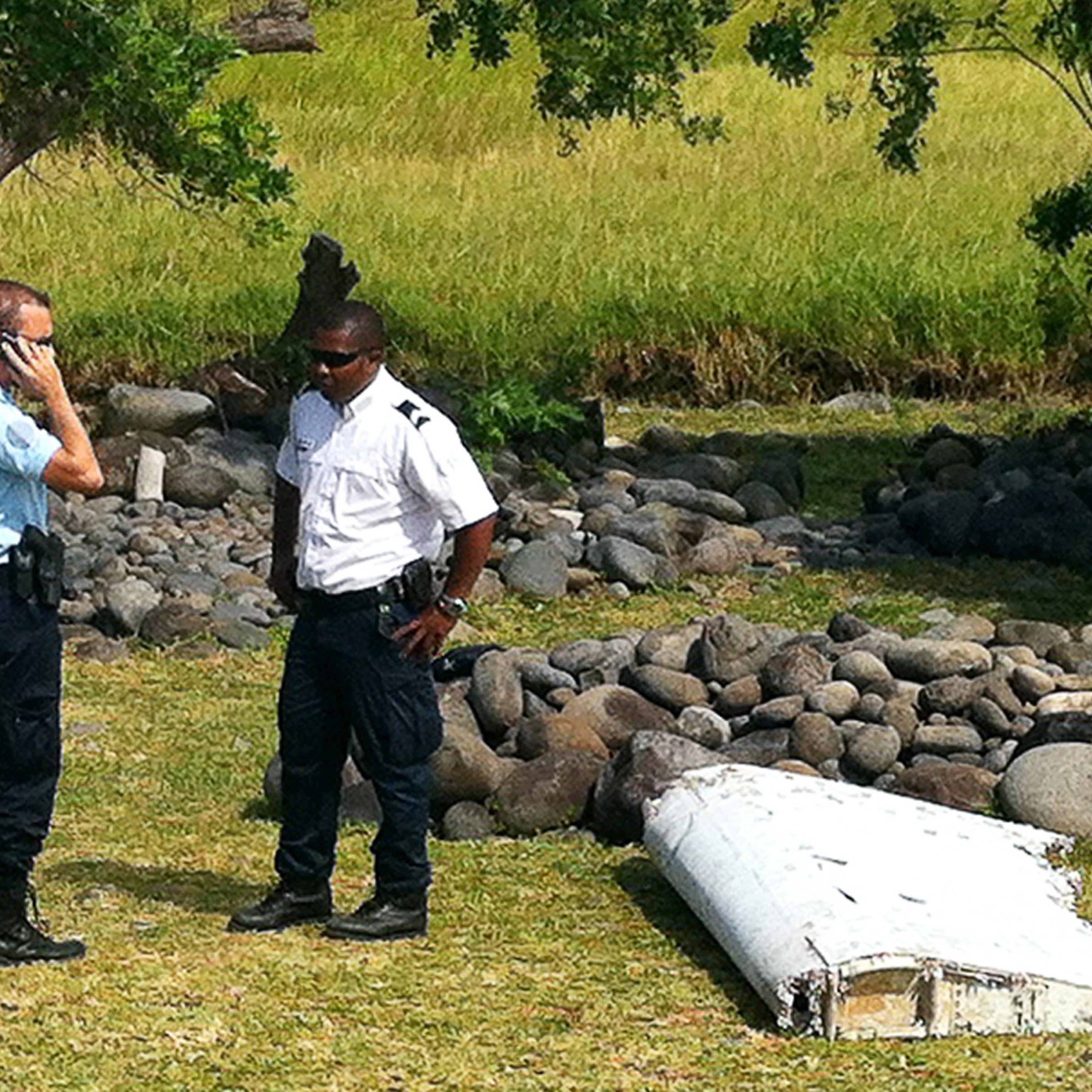A policeman and a gendarme stand next to a piece of debris from an unidentified aircraft found in the coastal area of Saint-Andre de la Reunion, in the east of the French Indian Ocean island of La Reunion, on July 29, 2015.