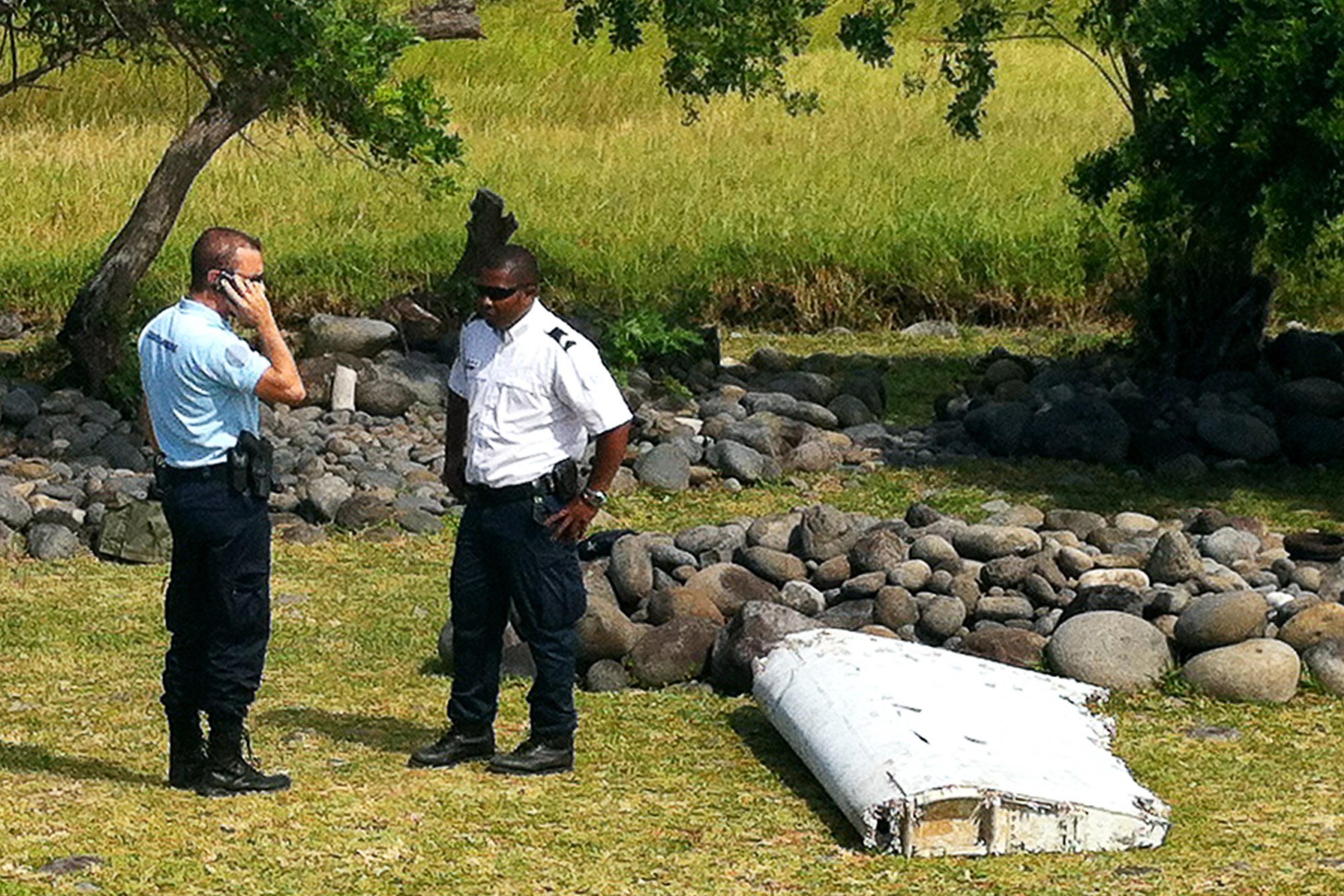 A policeman and a gendarme stand next to a piece of debris from an unidentified aircraft found in the coastal area of Saint-Andre de la Reunion, in the east of the French Indian Ocean island of La Reunion, on July 29, 2015.