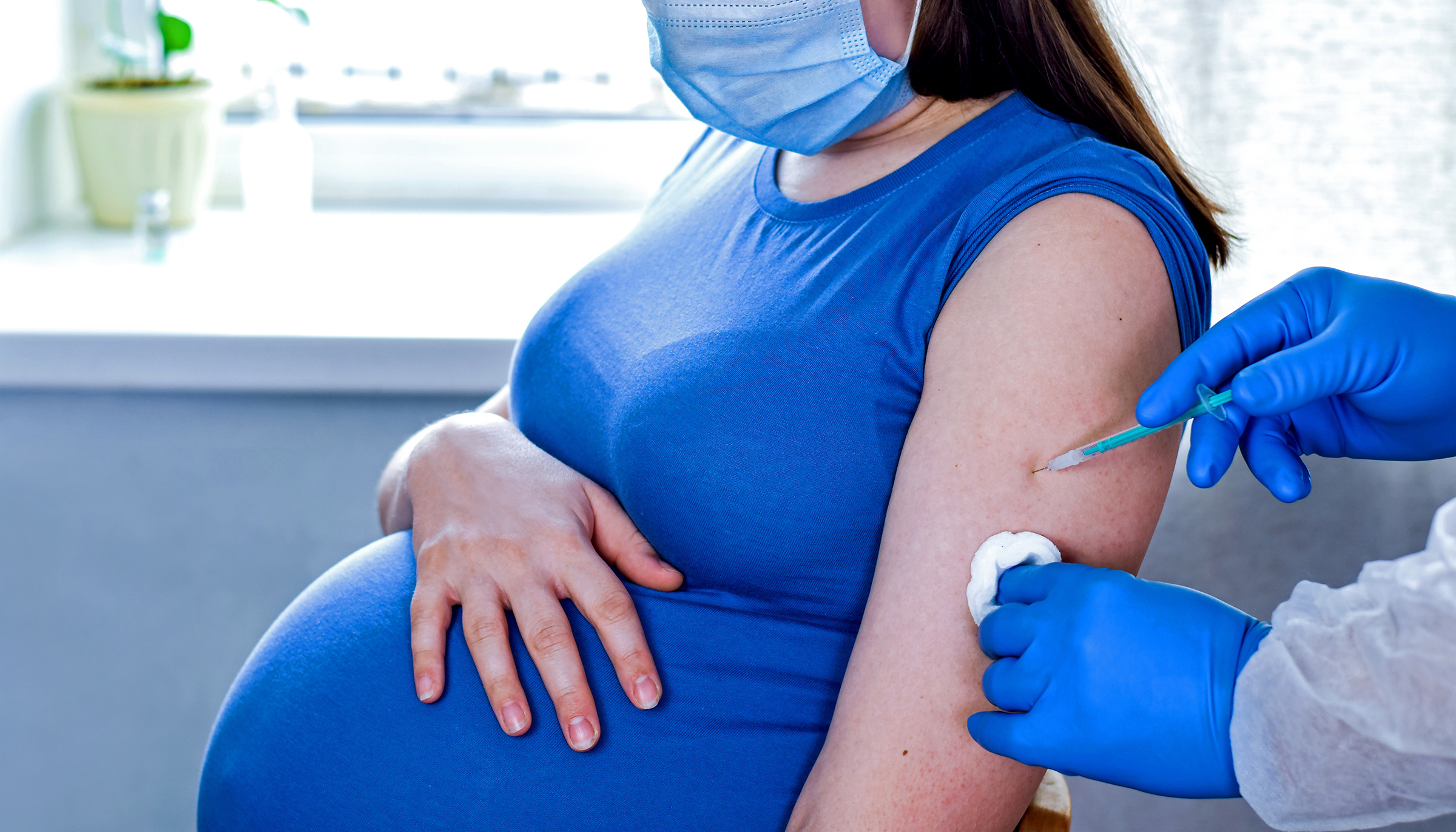 Doctor giving COVID -19 coronavirus vaccine injection to pregnant woman. Doctor Wearing Blue Gloves Vaccinating Young Pregnant Woman In Clinic. People vaccination concept.