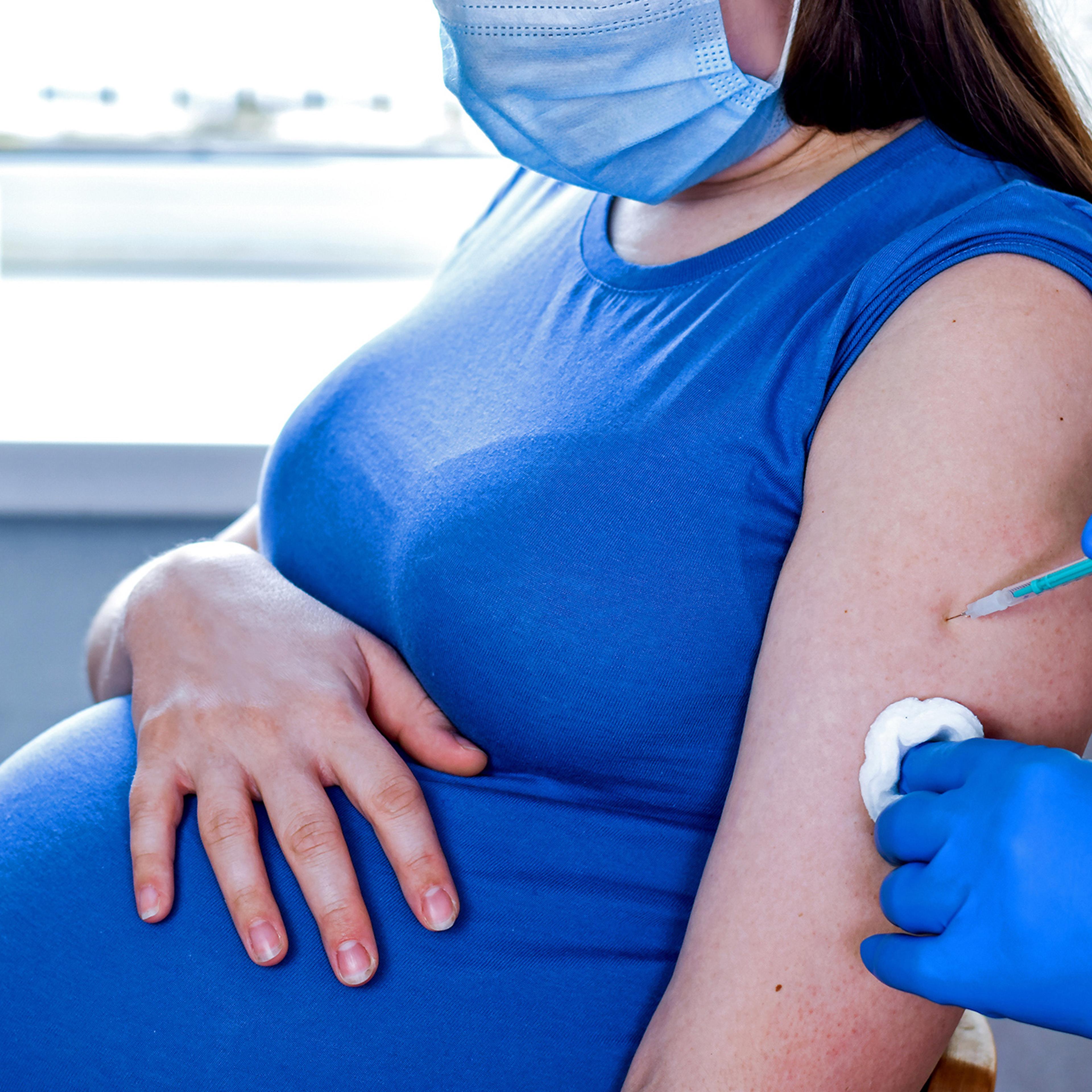 Doctor giving COVID -19 coronavirus vaccine injection to pregnant woman. Doctor Wearing Blue Gloves Vaccinating Young Pregnant Woman In Clinic. People vaccination concept.