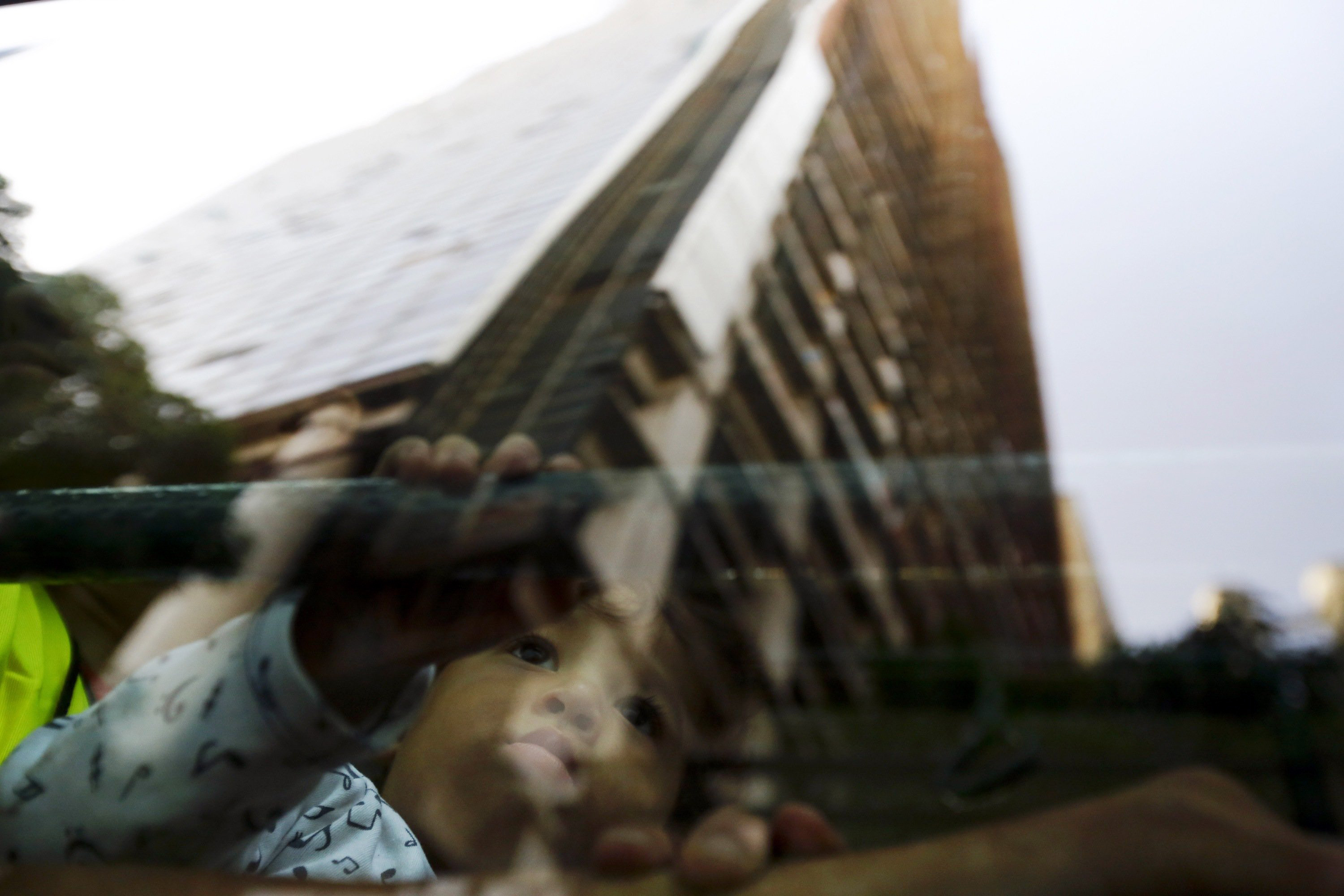 An evicted resident of Tower of David sits in a bus, as the building is reflected on the window, which will transport them to the new home in Caracas