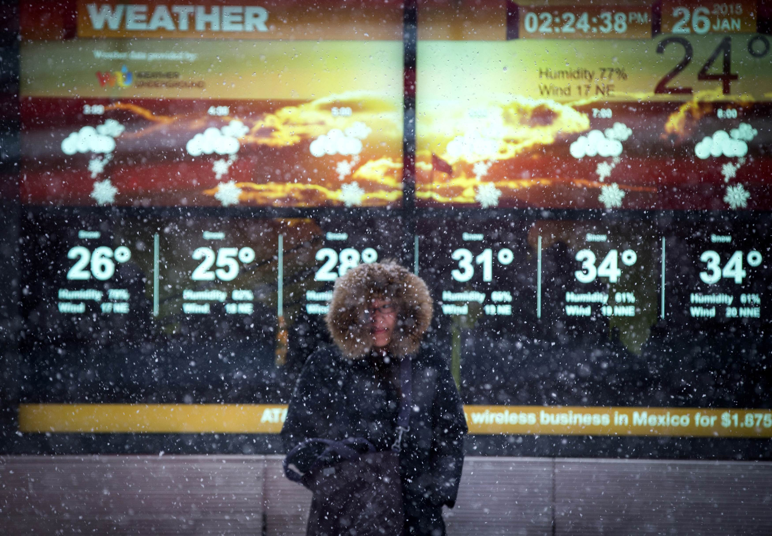 A woman stands in falling snow in front of an electronic sign displaying the weather forecast in Times Square in New York