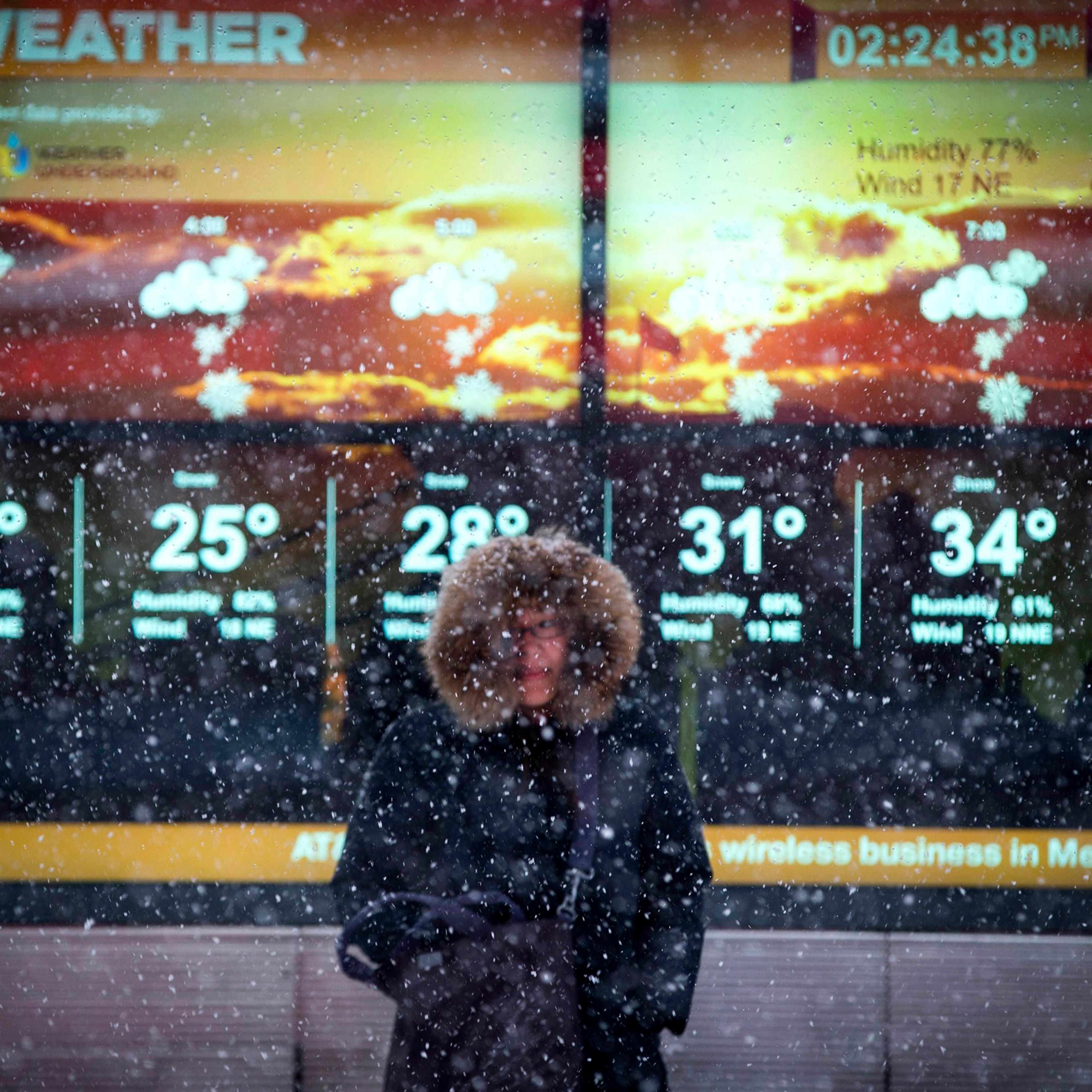 A woman stands in falling snow in front of an electronic sign displaying the weather forecast in Times Square in New York