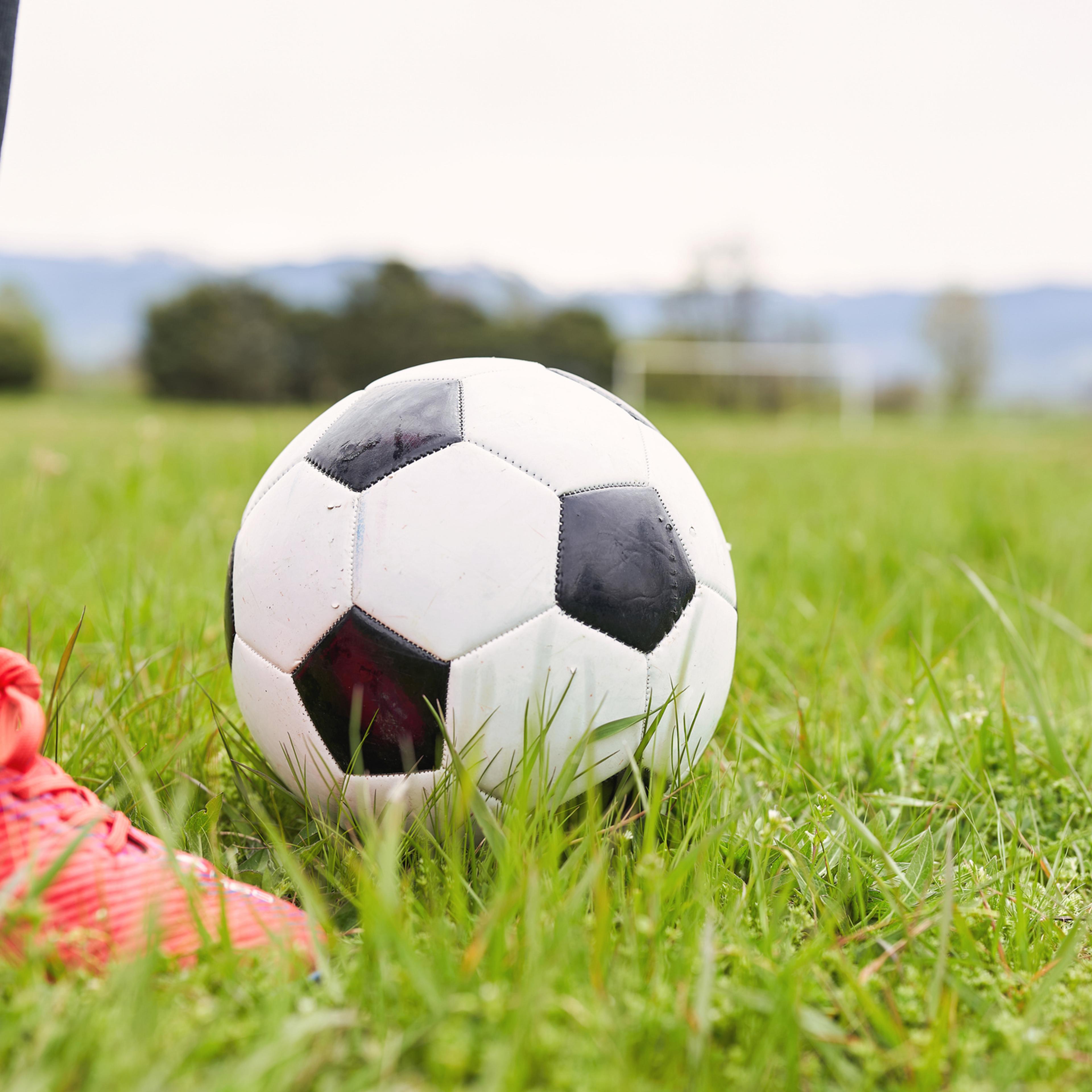 Closeup of soccer ball on grassy field next to player in red shoes