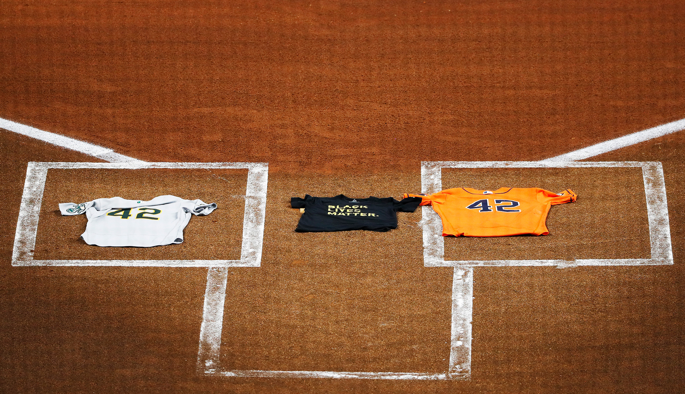 An Oakland Athletics jersey, laid by Marcus Semien, and a Houston Astros jersey, laid by Martin Maldonado, both bearing the No. 42 in honor of Jackie Robinson, flank a Black Lives Matter T-shirt covering home plate in Houston on Aug. 28