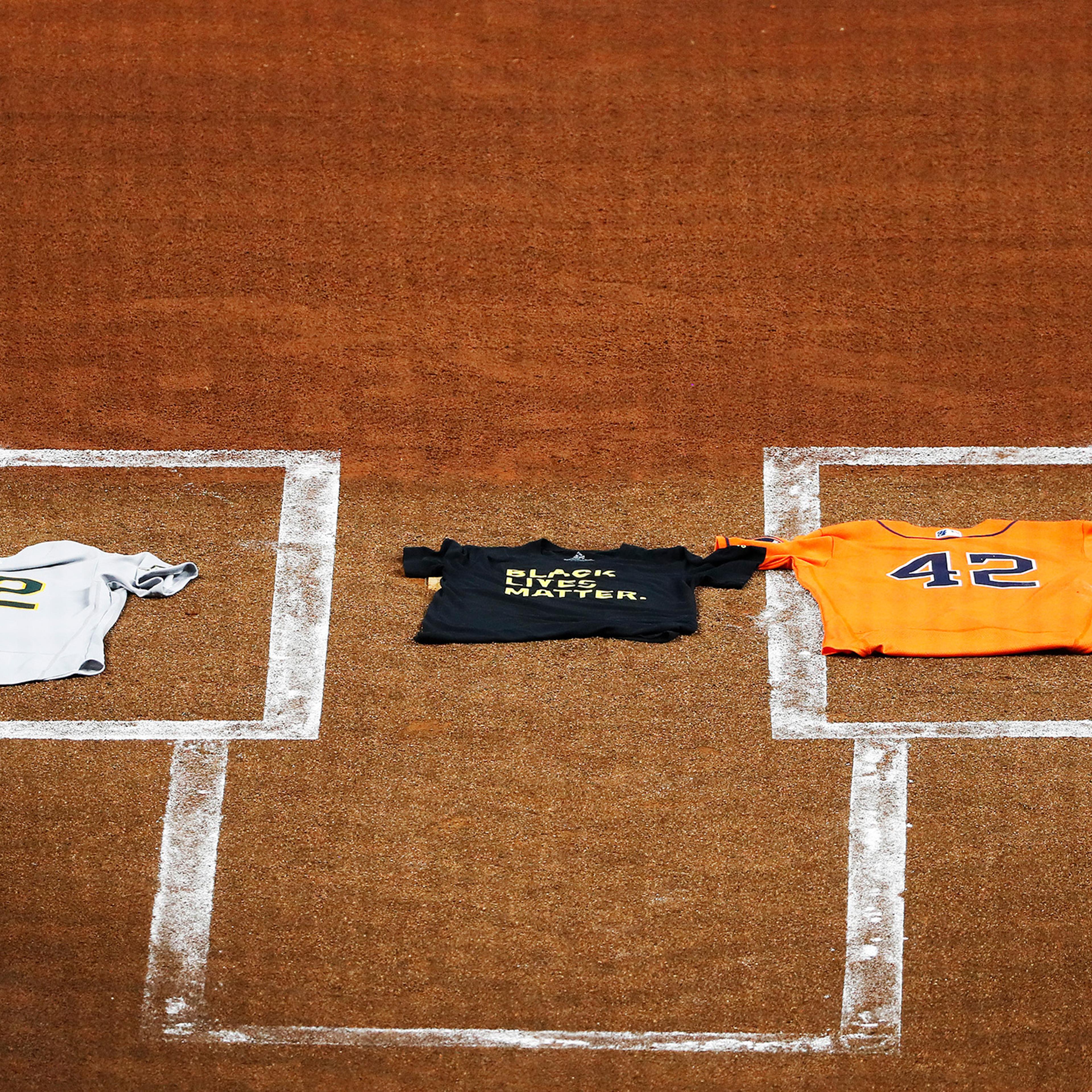 An Oakland Athletics jersey, laid by Marcus Semien, and a Houston Astros jersey, laid by Martin Maldonado, both bearing the No. 42 in honor of Jackie Robinson, flank a Black Lives Matter T-shirt covering home plate in Houston on Aug. 28