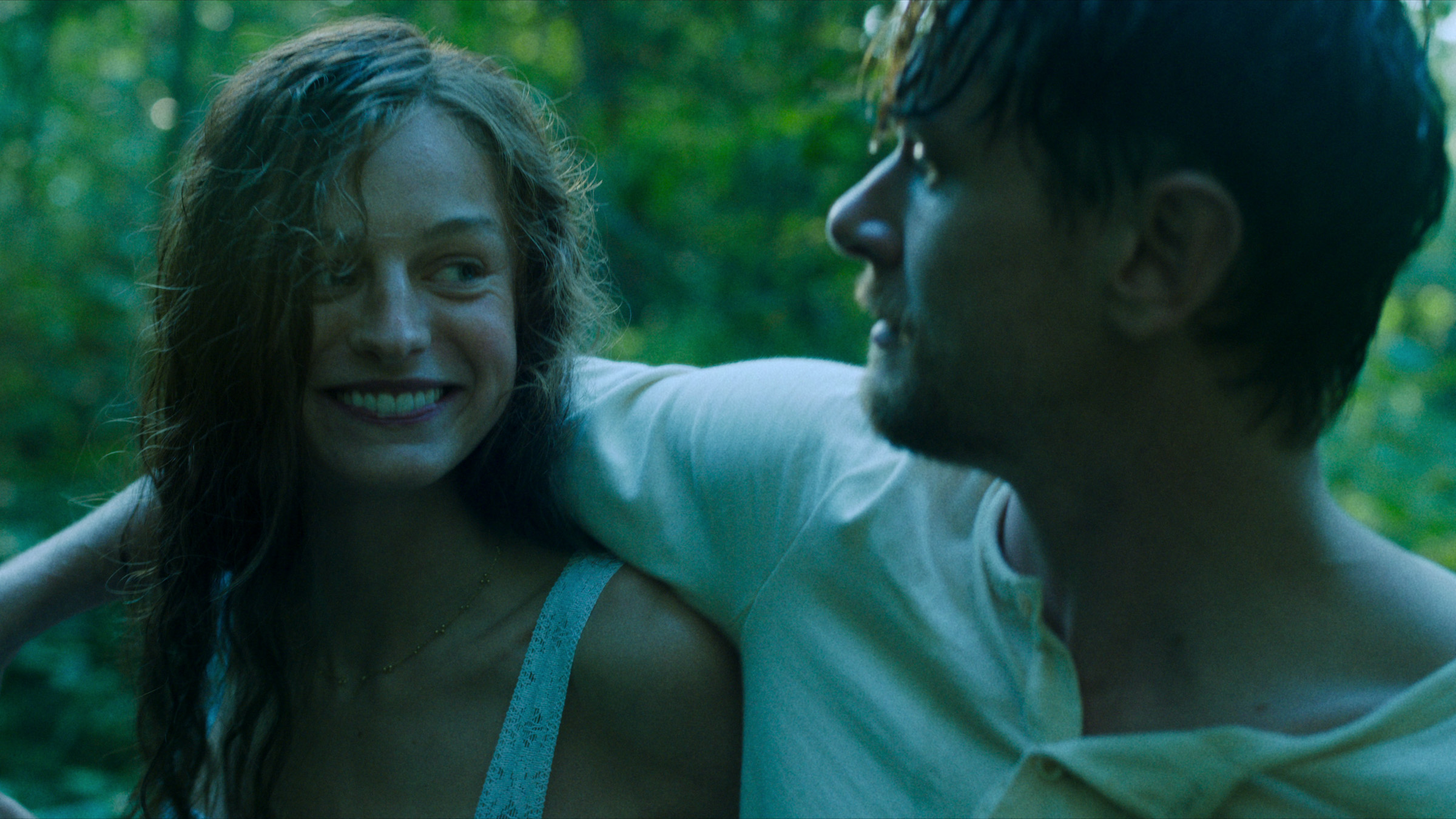 Jack O'Connell slings his arm over the shoulder of Emma Corrin, who is beaming at him.