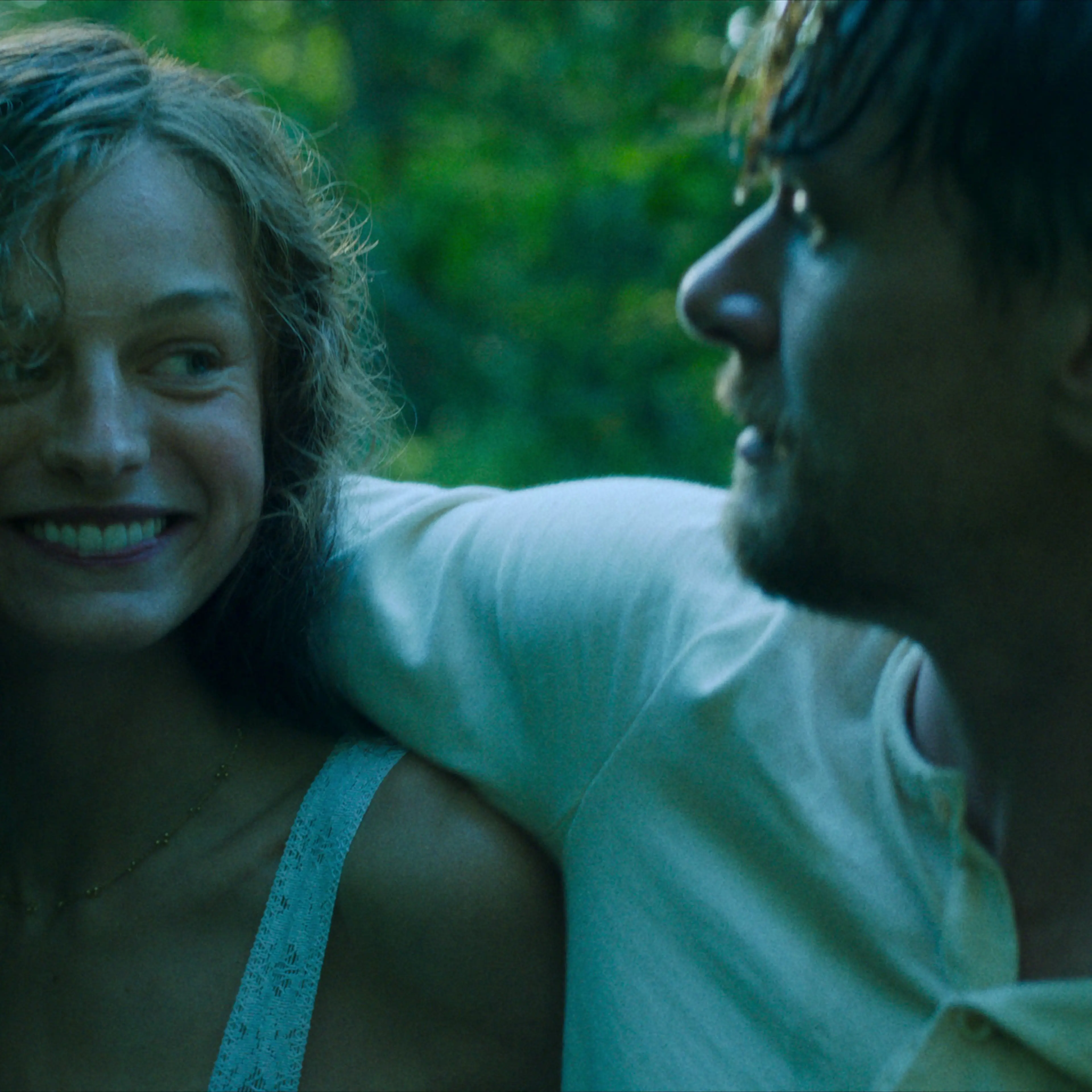 Jack O'Connell slings his arm over the shoulder of Emma Corrin, who is beaming at him.