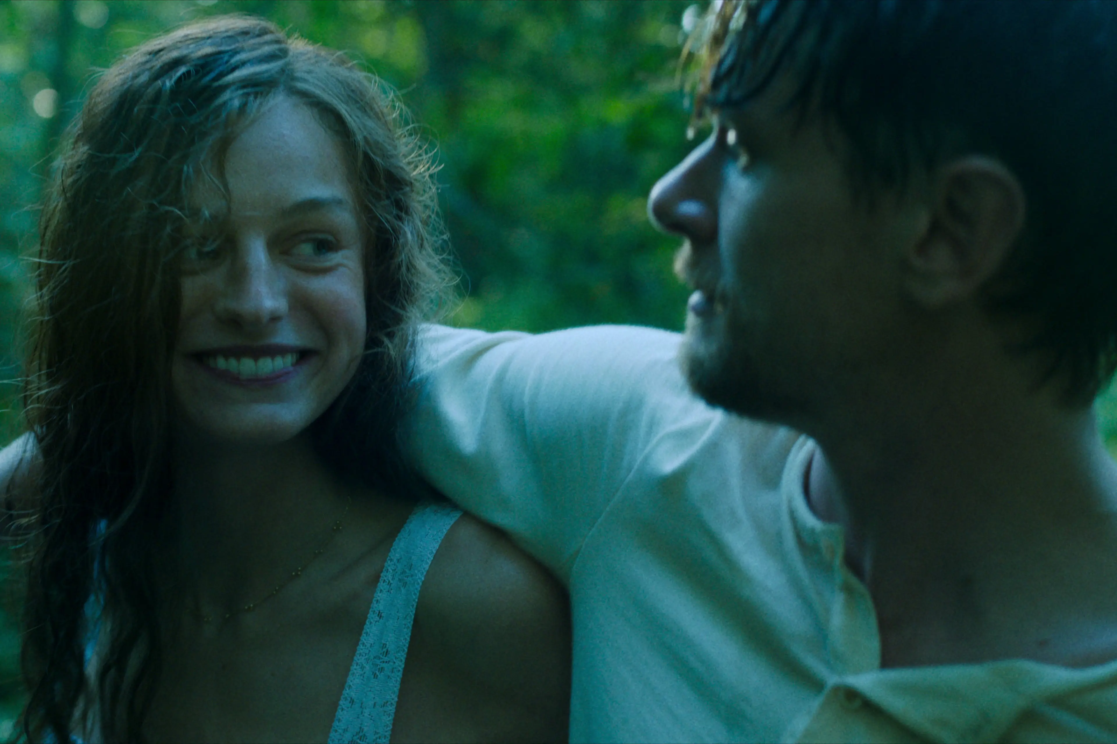 Jack O'Connell slings his arm over the shoulder of Emma Corrin, who is beaming at him.