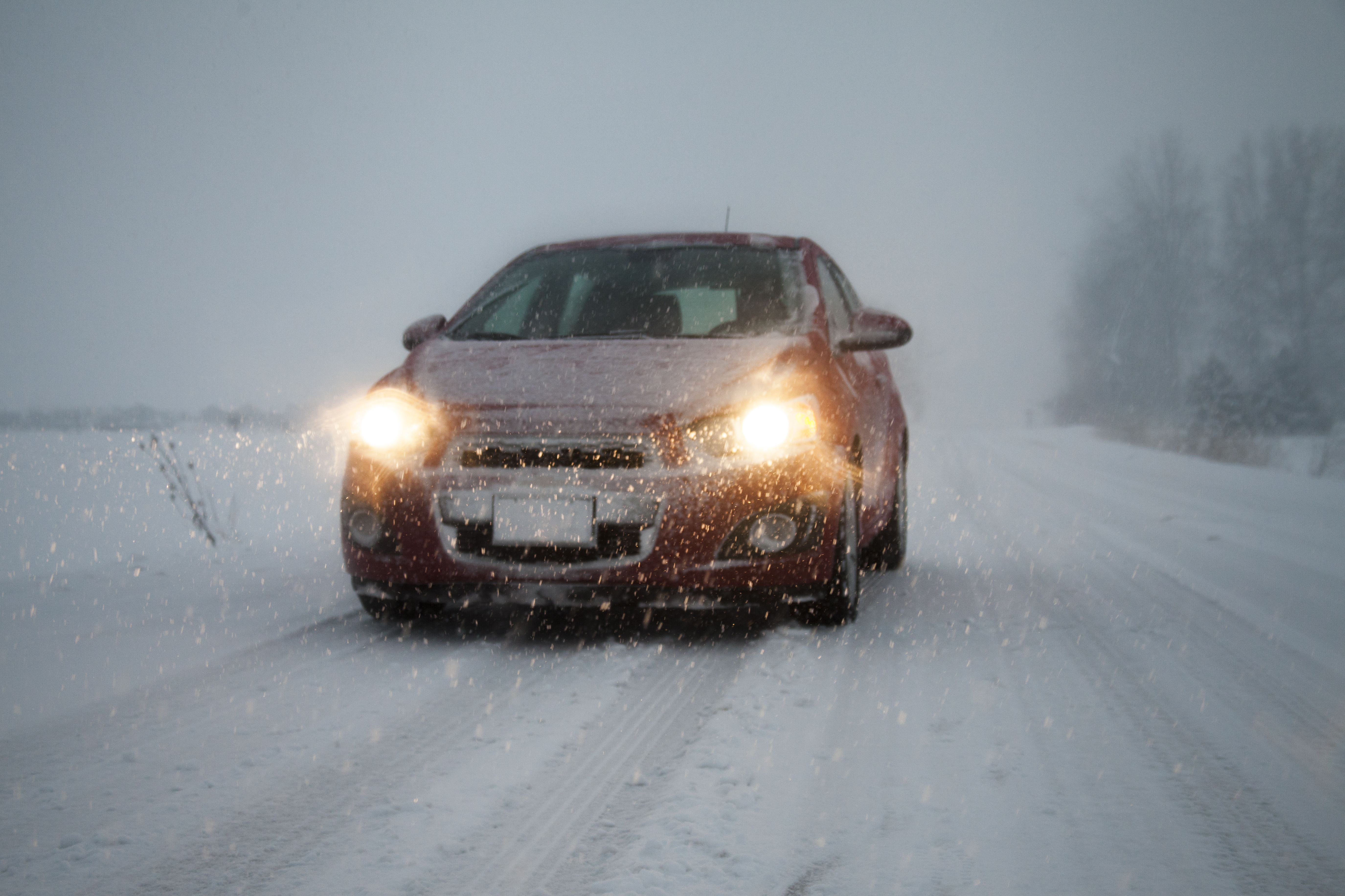 Car with headlights on driving along foggy snow covered road