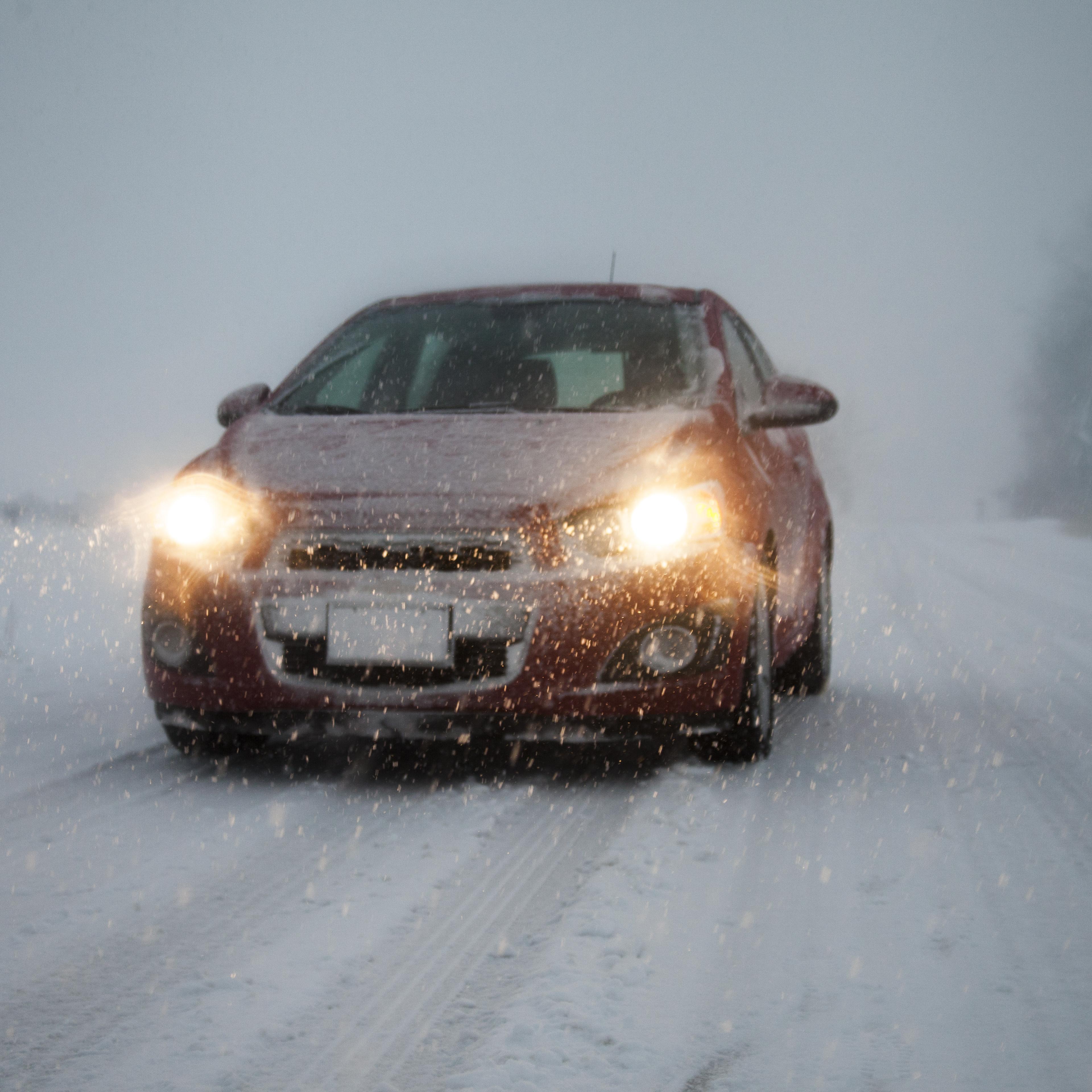 Car with headlights on driving along foggy snow covered road