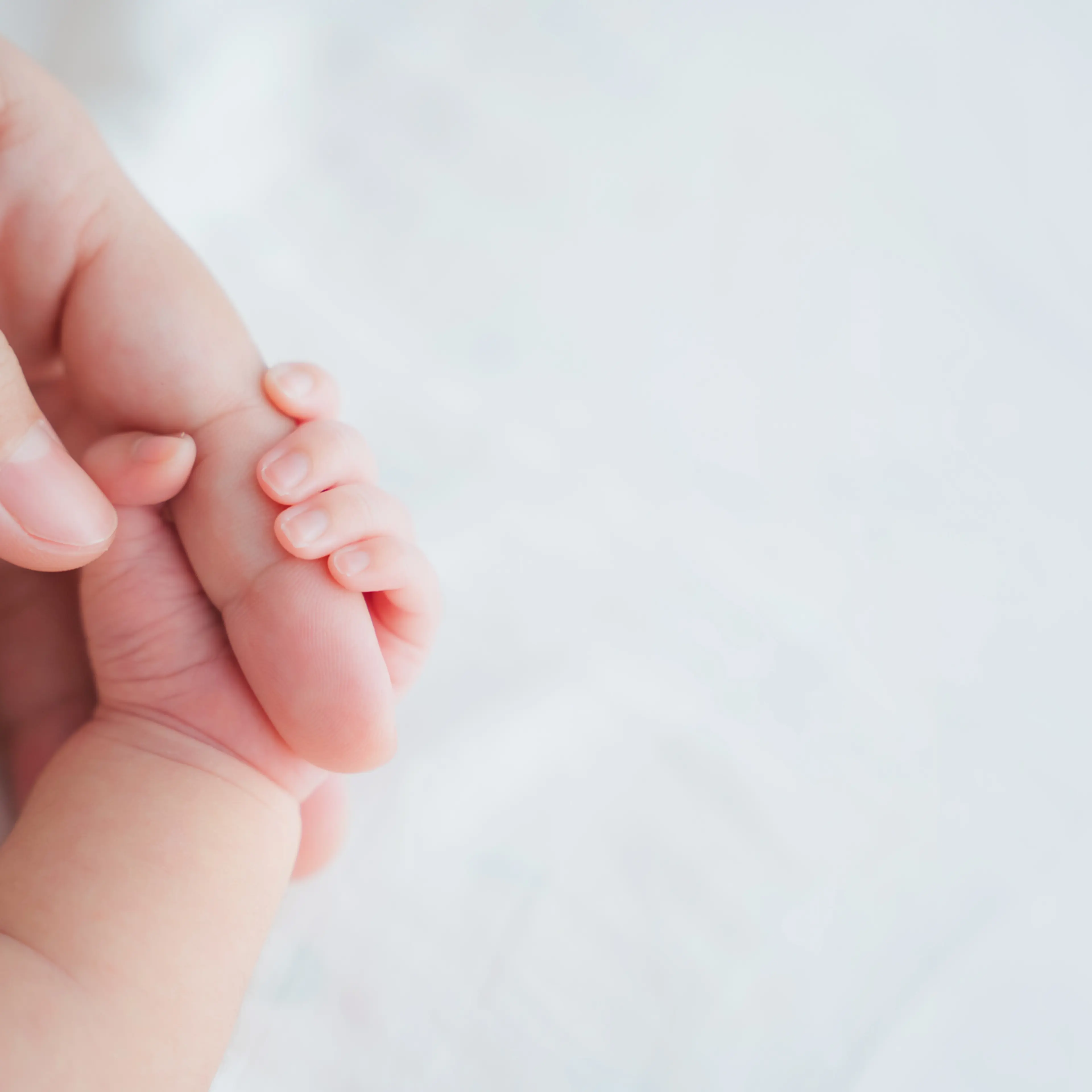 Mother uses her hand to hold her baby's tiny hand to make him feeling her love, warm and secure. Newborn.