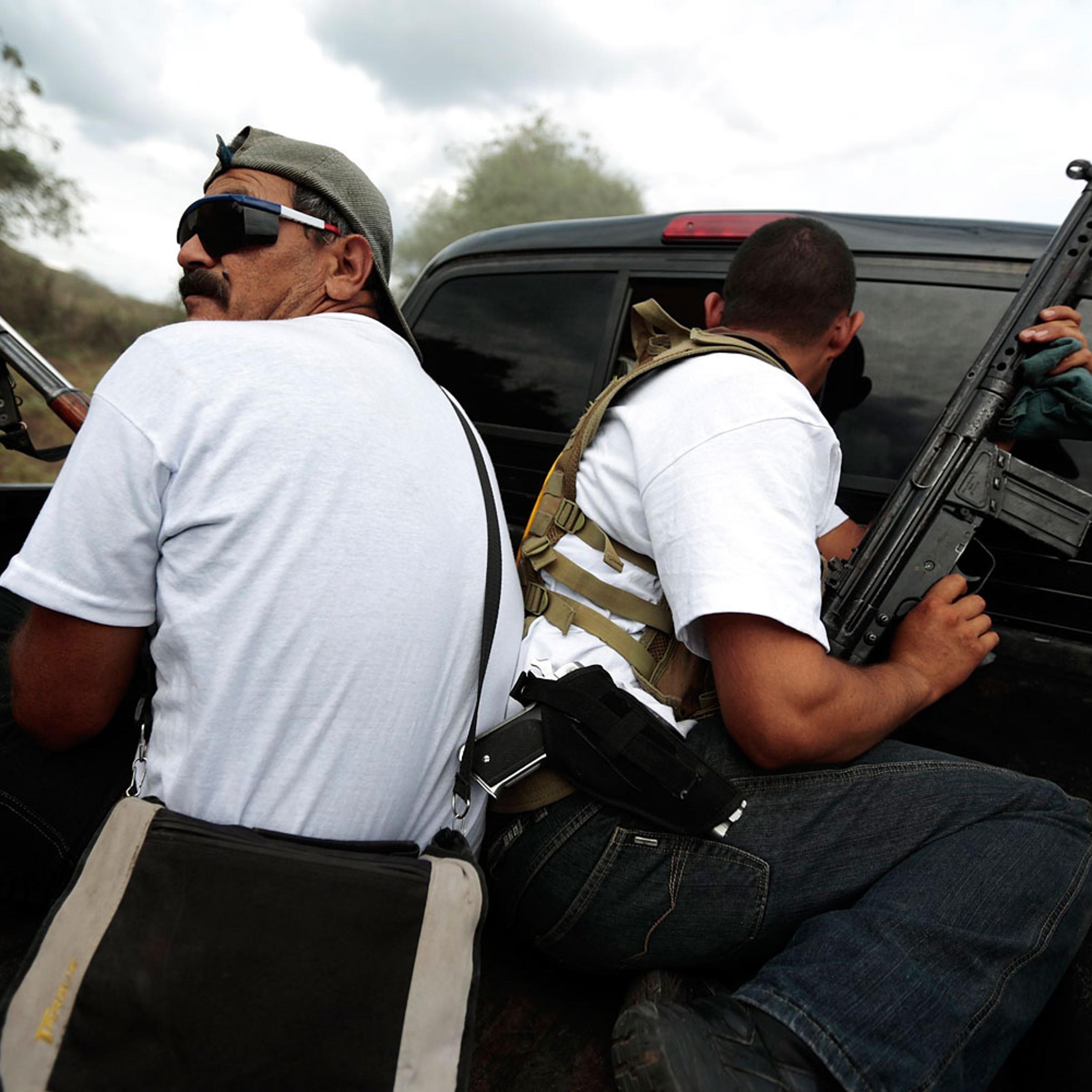 Vigilantes ride on the back of a pick-up truck while driving in a convoy to Poturo, Michoacan, Dec. 29, 2013.