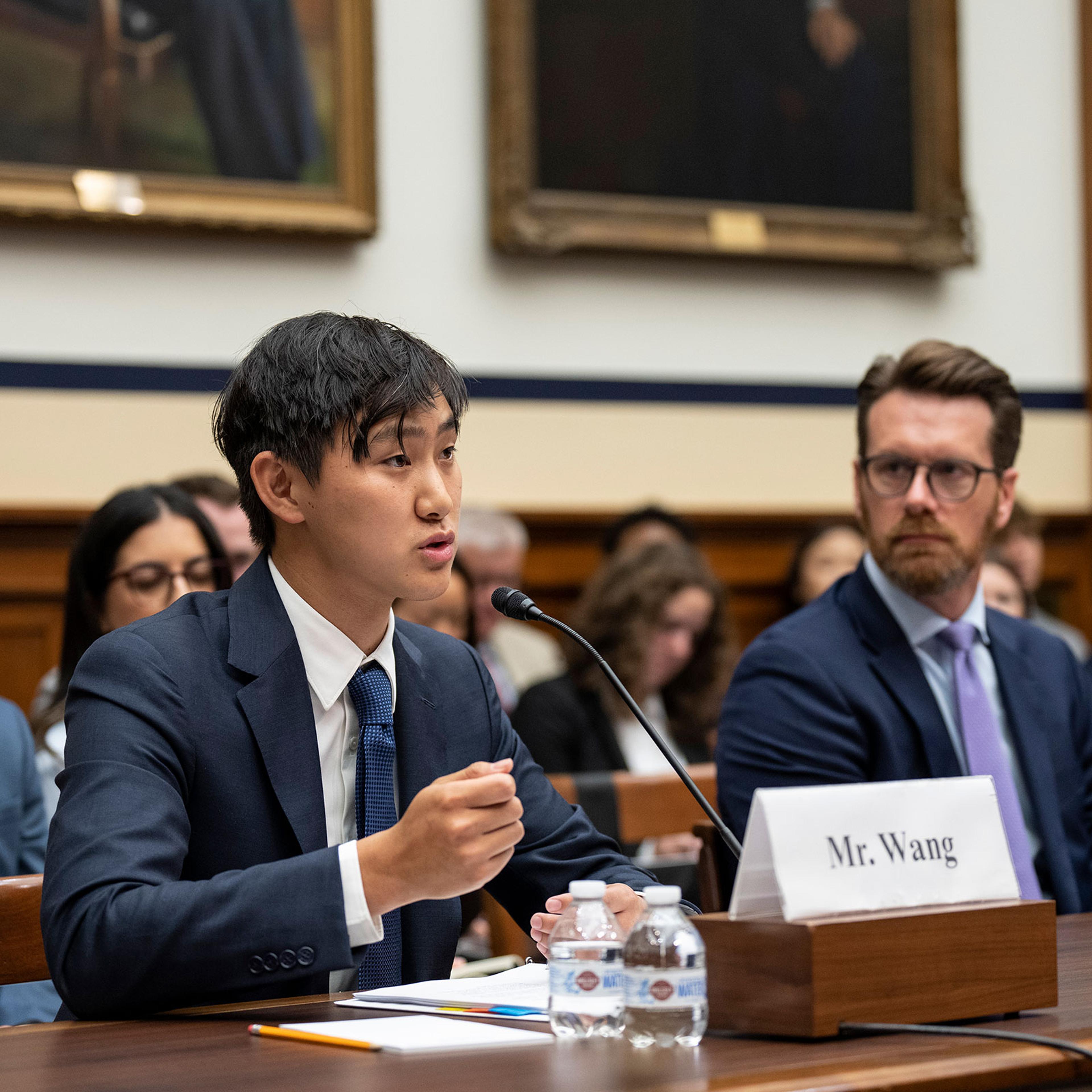 CEO of Scale A.I. Alexandr Wang behind a table speaking into a microphone during testimony