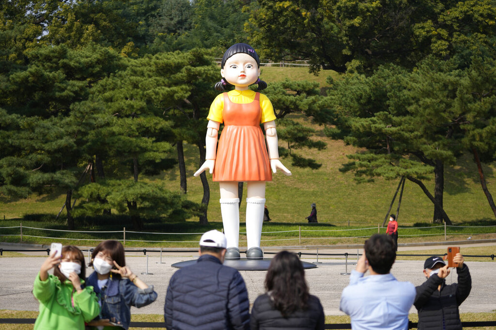 Visitors take photos of a model of the massive doll that was featured in Netflix’s series "Squid Game" displayed at the Olympic Park in Seoul, Oct. 26, 2021.