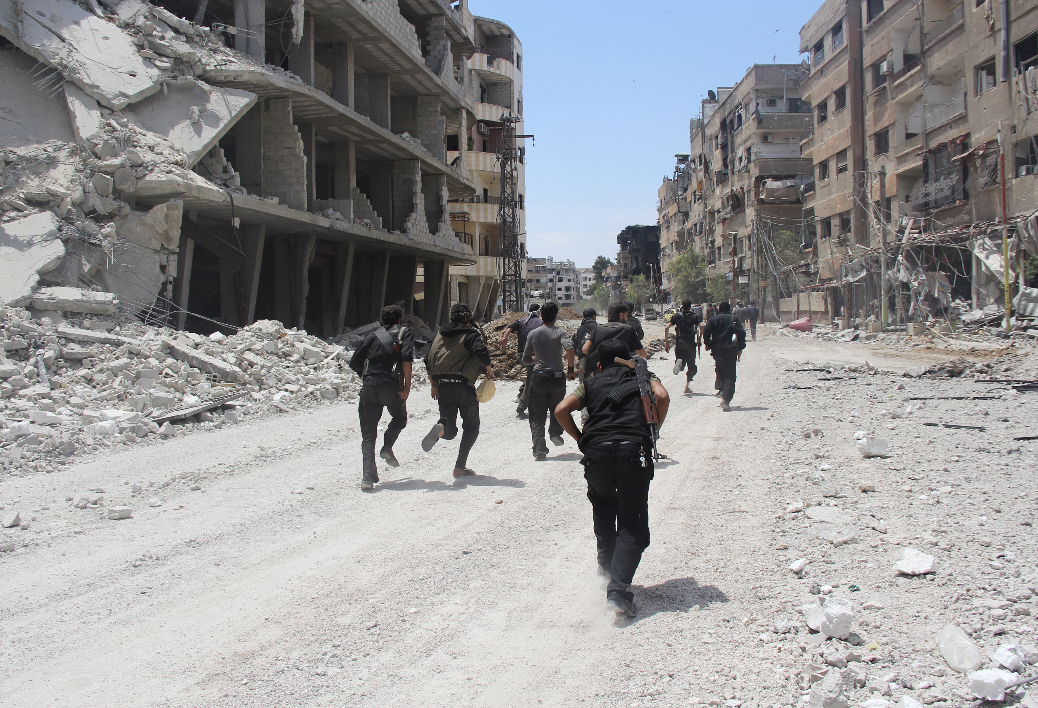 Rebel fighters carry their weapons as they run past damaged buildings to avoid snipers loyal to Syria's President Bashar al-Assad in the Mleha suburb of Damascus May 26, 2014. REUTERS/Badra Mamet (SYRIA - Tags: POLITICS CIVIL UNREST CONFLICT MILITARY) - RTR3QXRJ