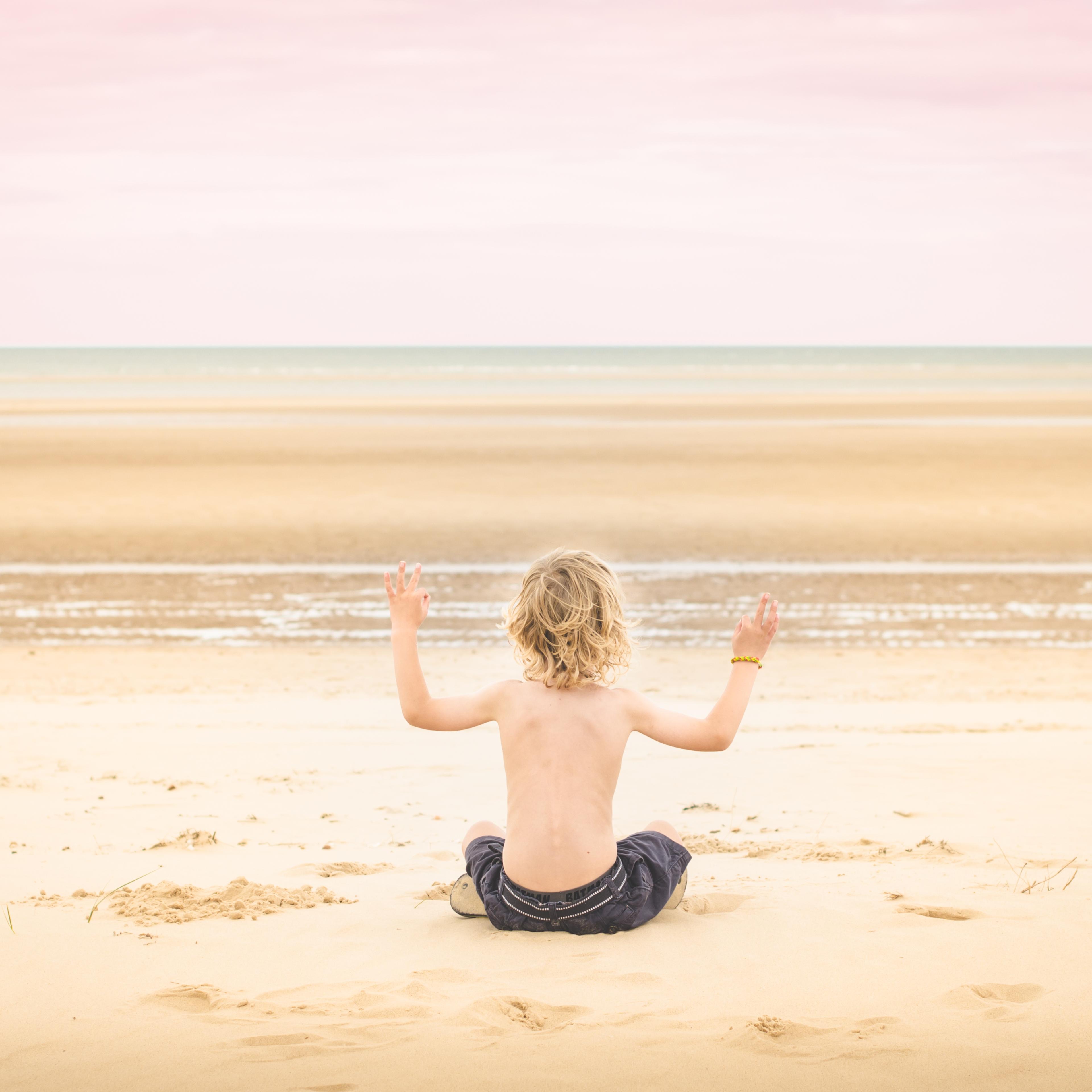 Boy sitting on beach, arms raised