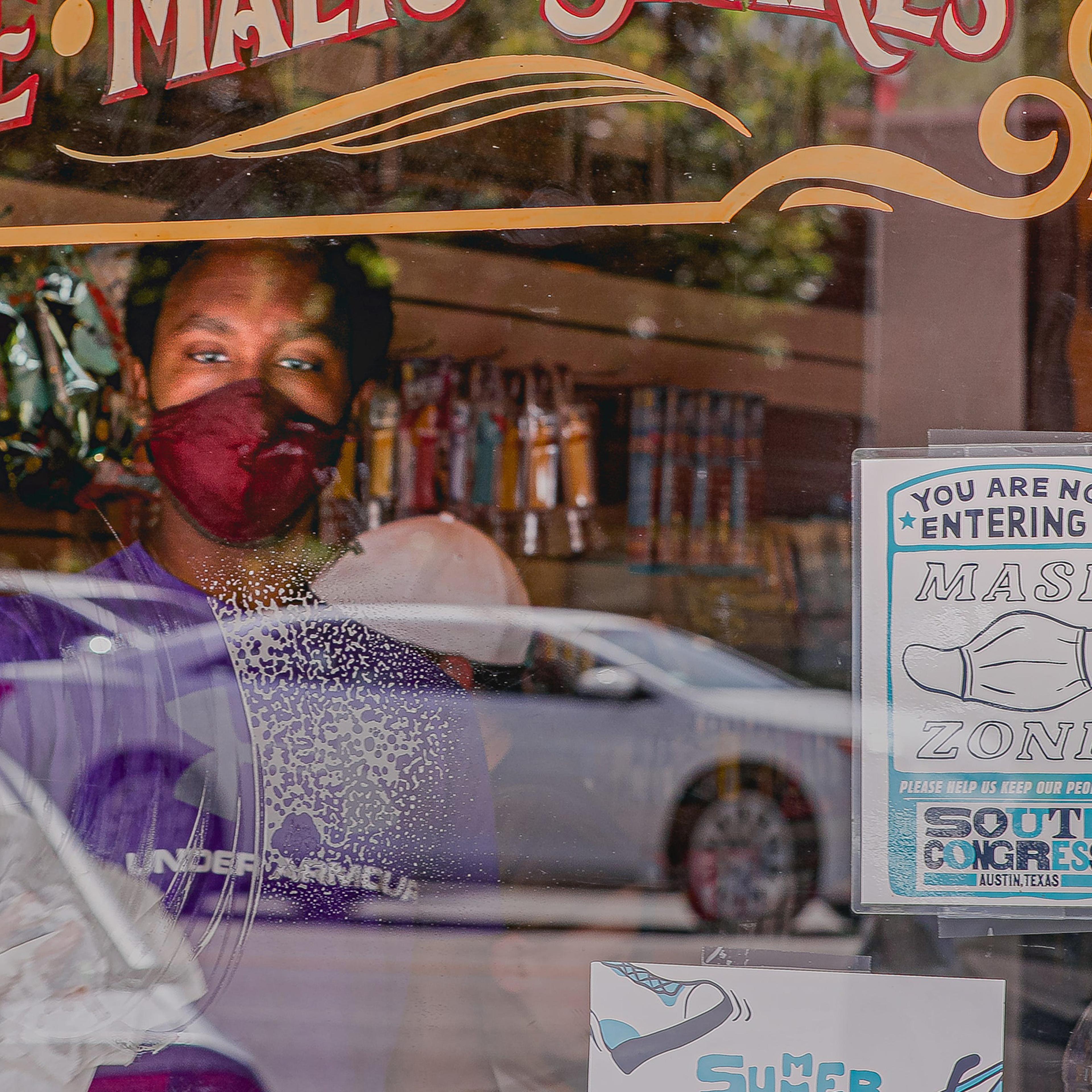 A store employee wearing a mask cleans a window with a sign requesting customers put on masks at a shop on Austin's South Congress Avenue on Sept. 30.