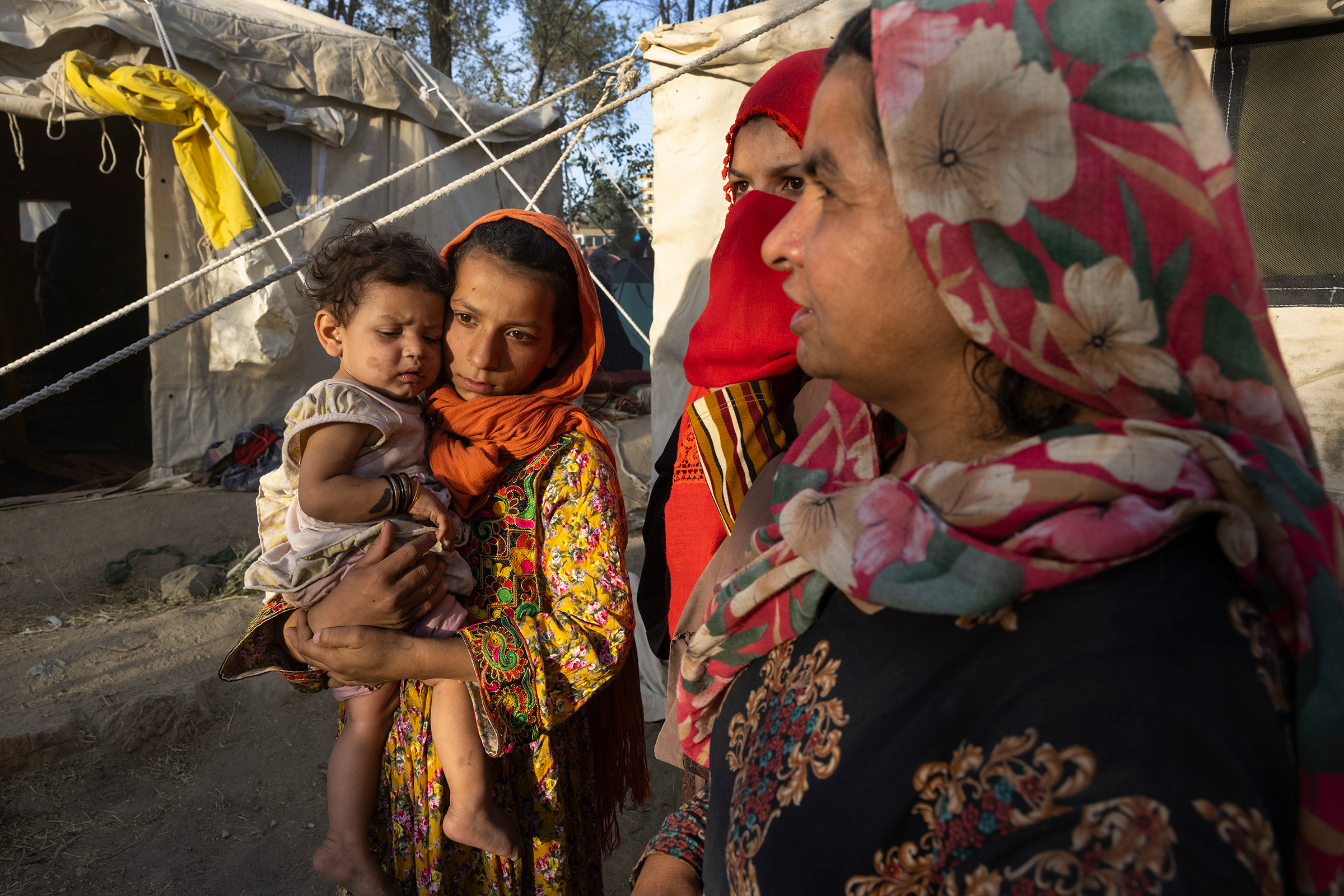 Halida, an 11-year-old whose father was killed by the Taliban, holds her eight-month-old cousin, Shafika, alongside family members as Afghans from the northern provinces arrive at a makeshift camp in Kabul on Aug. 10, 2021. Five days later, the Taliban t