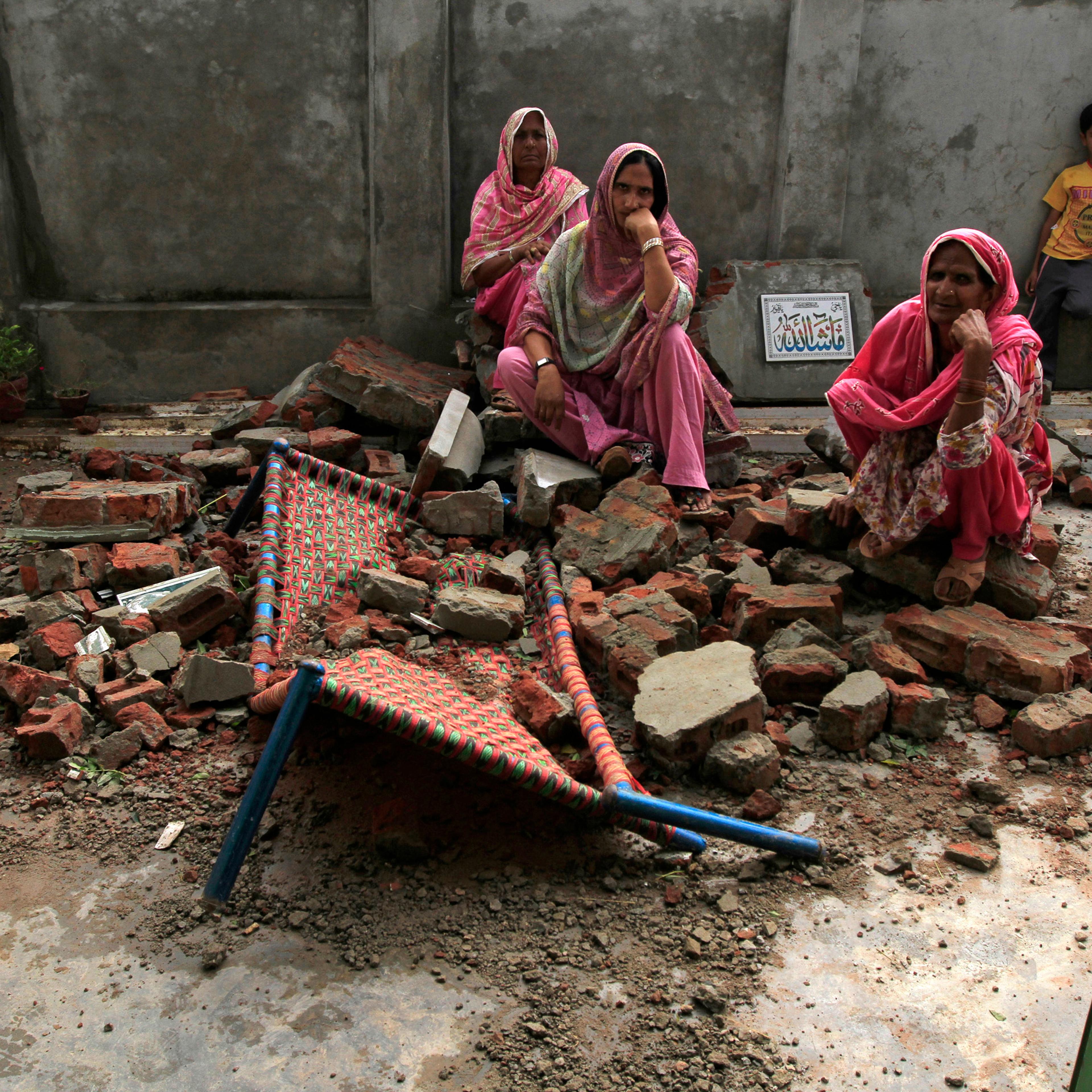 Villagers sit on the debris of their house after it was damaged during the recent exchange of fire between Pakistan and India at the Pakistani border town of Dhamala Hakimwala