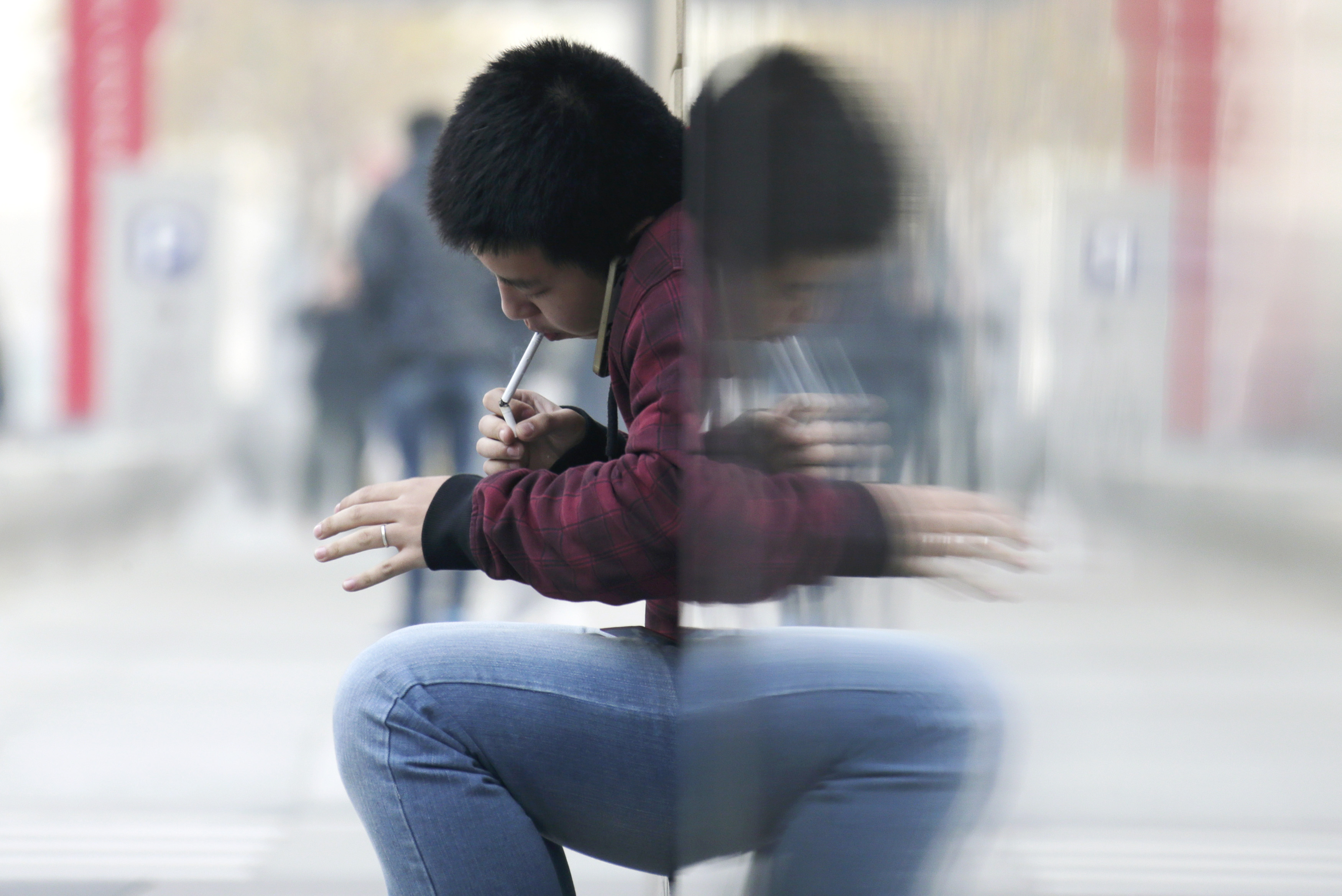 Man lights up a cigarette with another cigarette outside an office building in Beijing