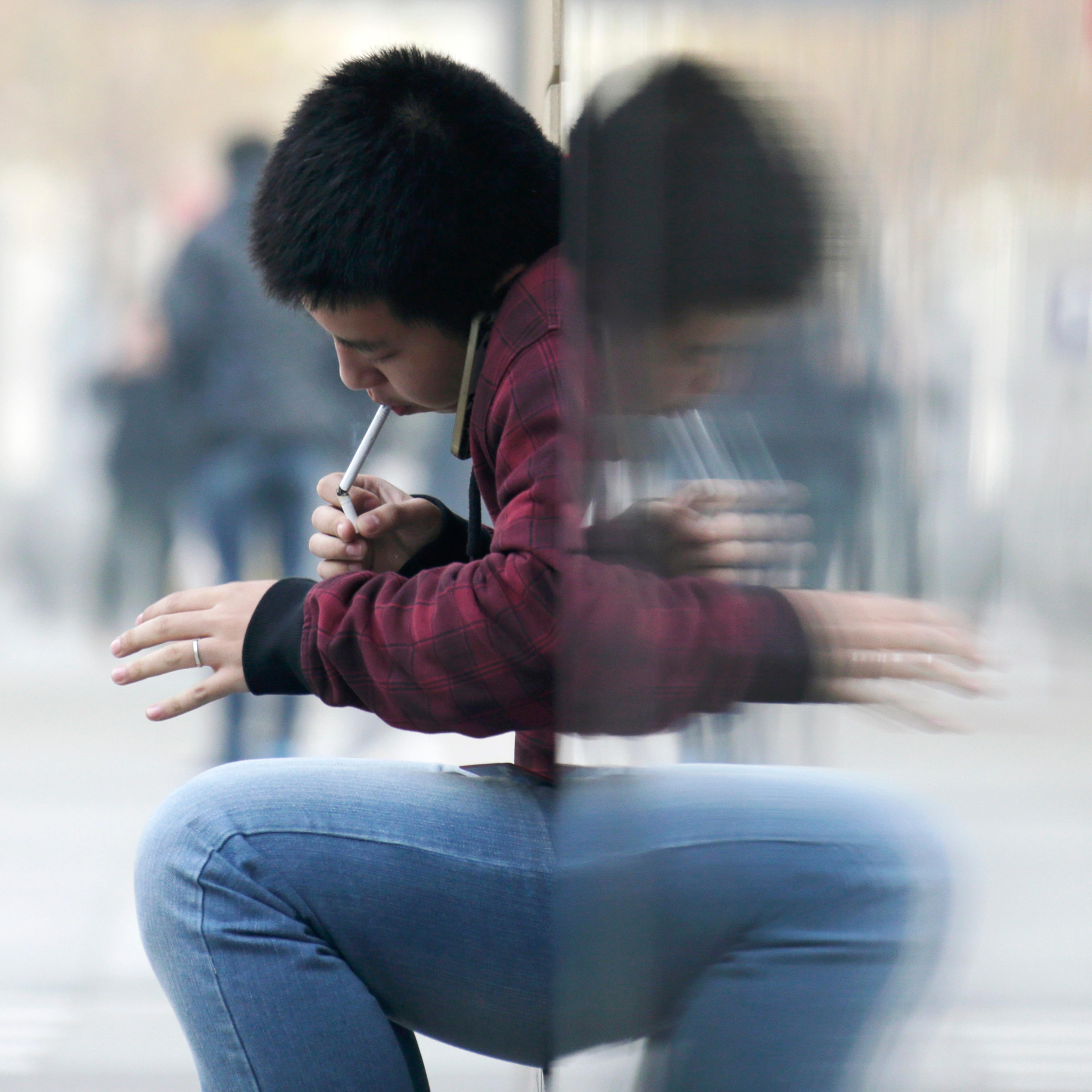 Man lights up a cigarette with another cigarette outside an office building in Beijing