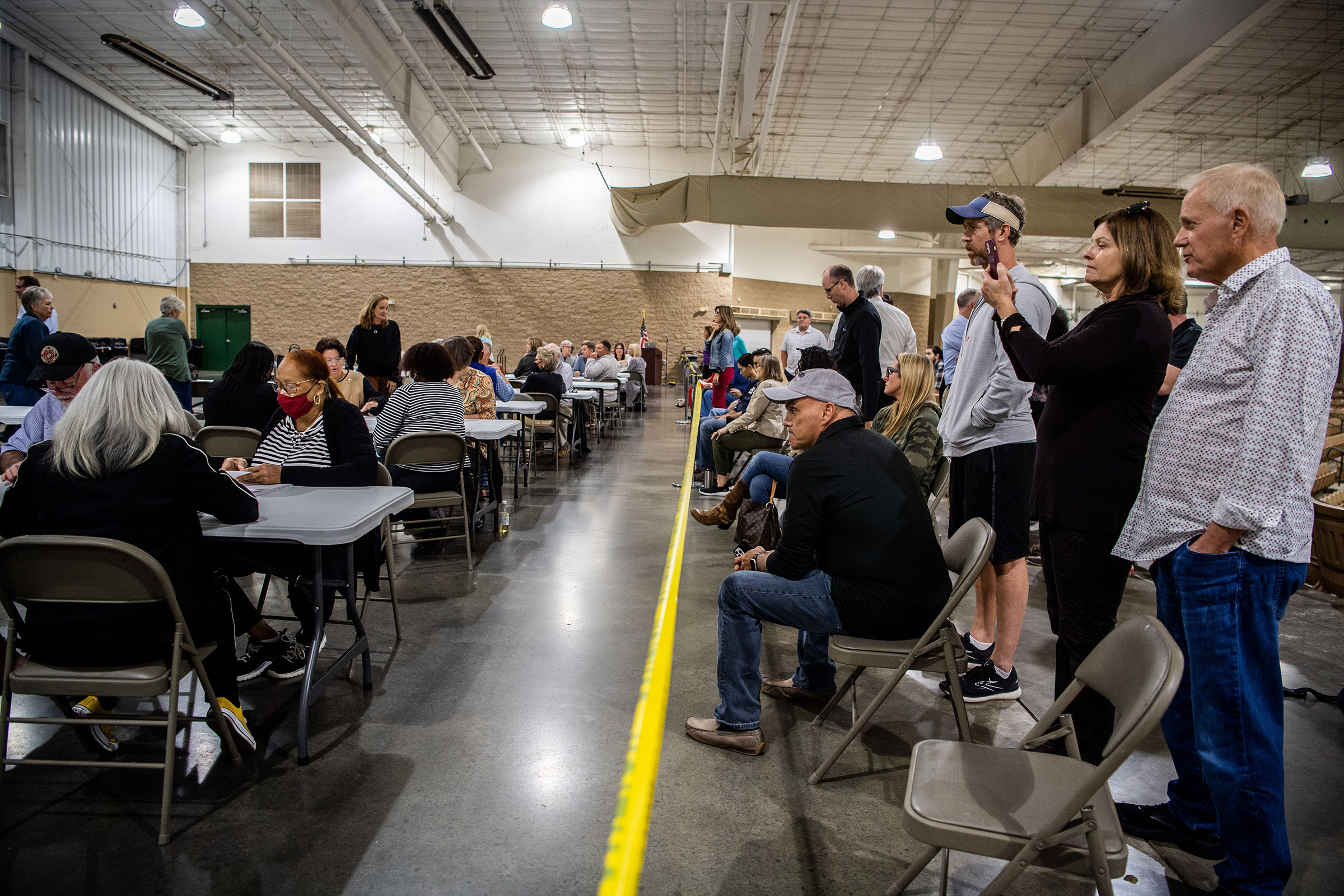 Poll watchers stand behind the yellow tape as poll officials count the ballots by hand, due to software issues with the voting machine tabulators, in Franklin, Tenn., on Oct. 27, 2021.