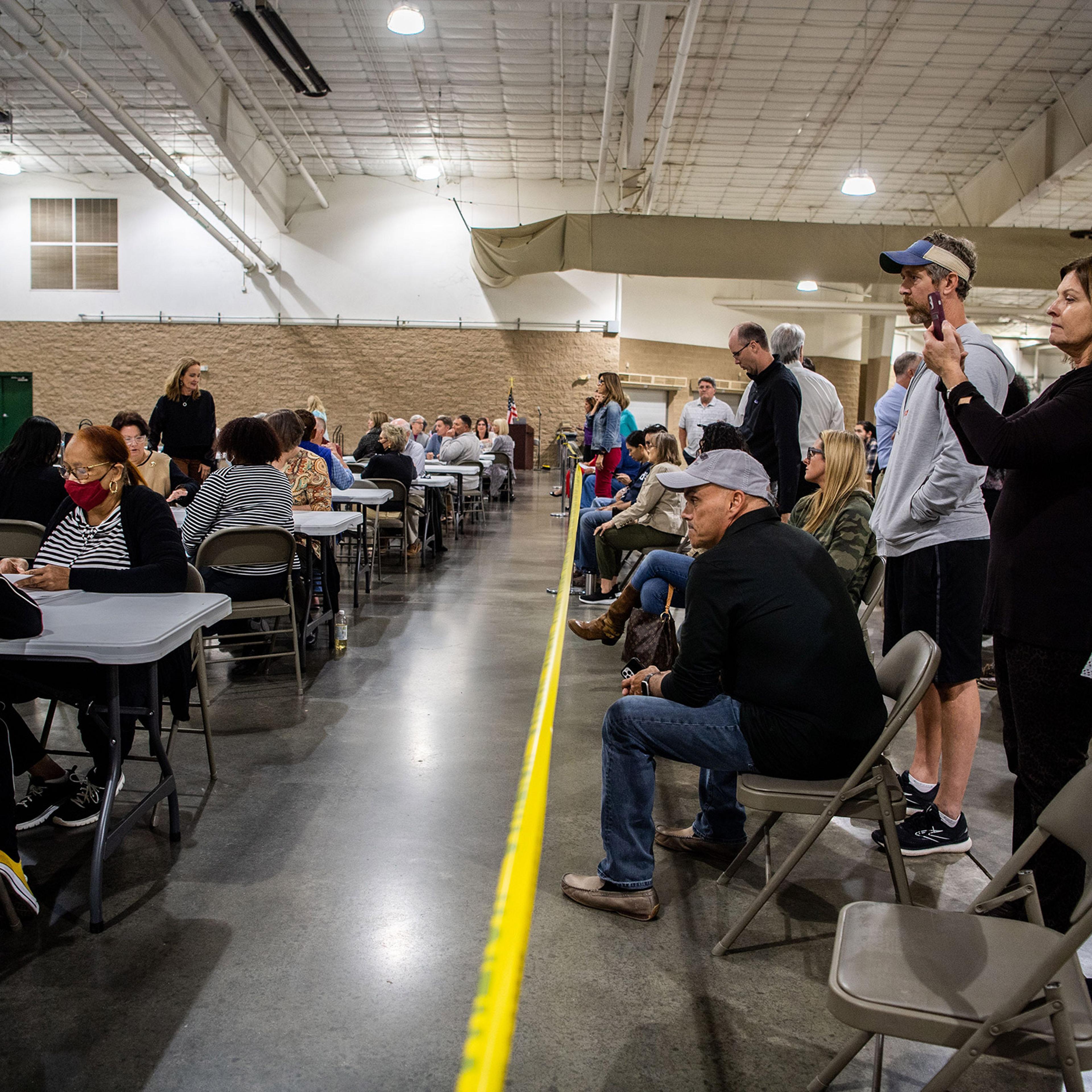 Poll watchers stand behind the yellow tape as poll officials count the ballots by hand, due to software issues with the voting machine tabulators, in Franklin, Tenn., on Oct. 27, 2021.