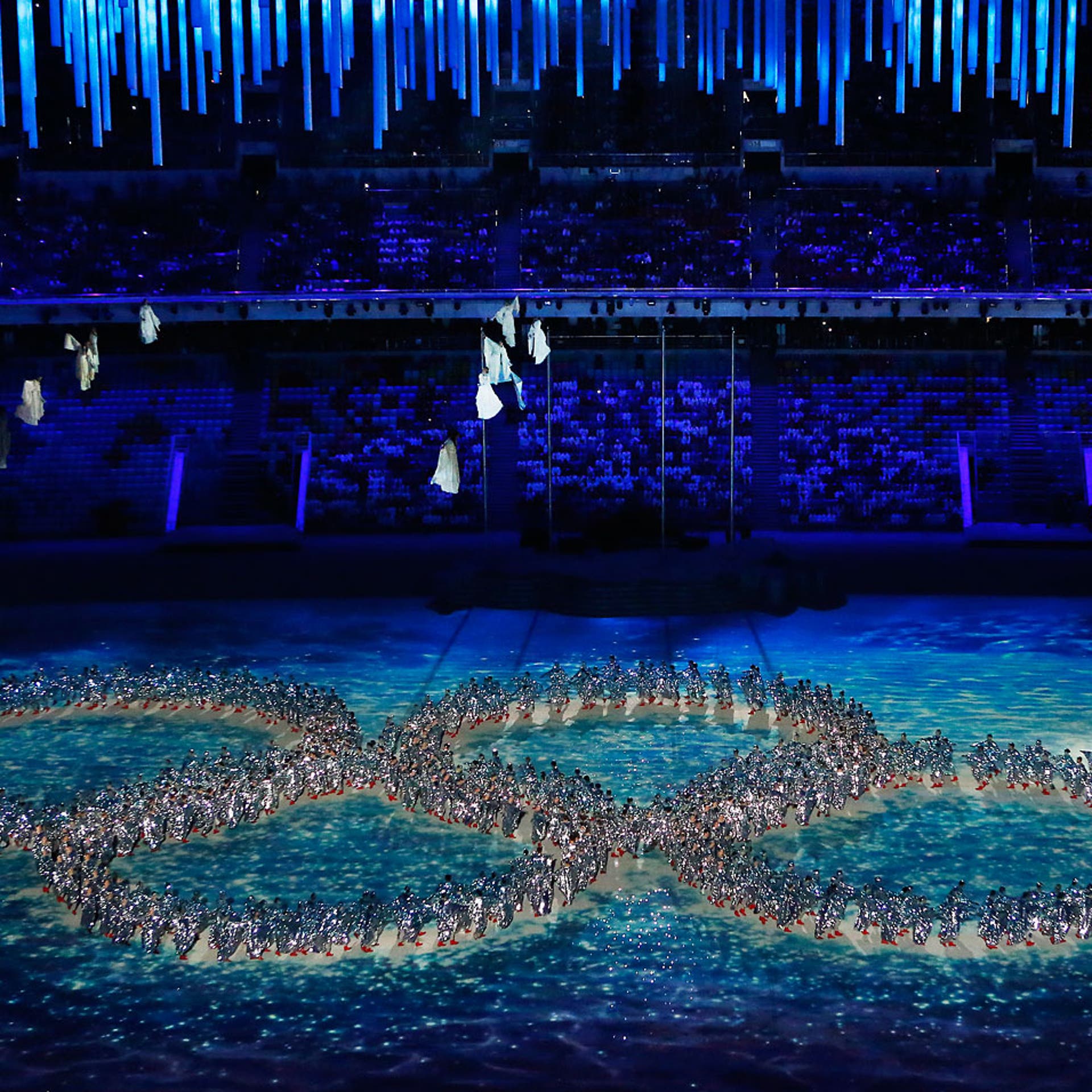 Dancers create the incomplete Olympic Rings.