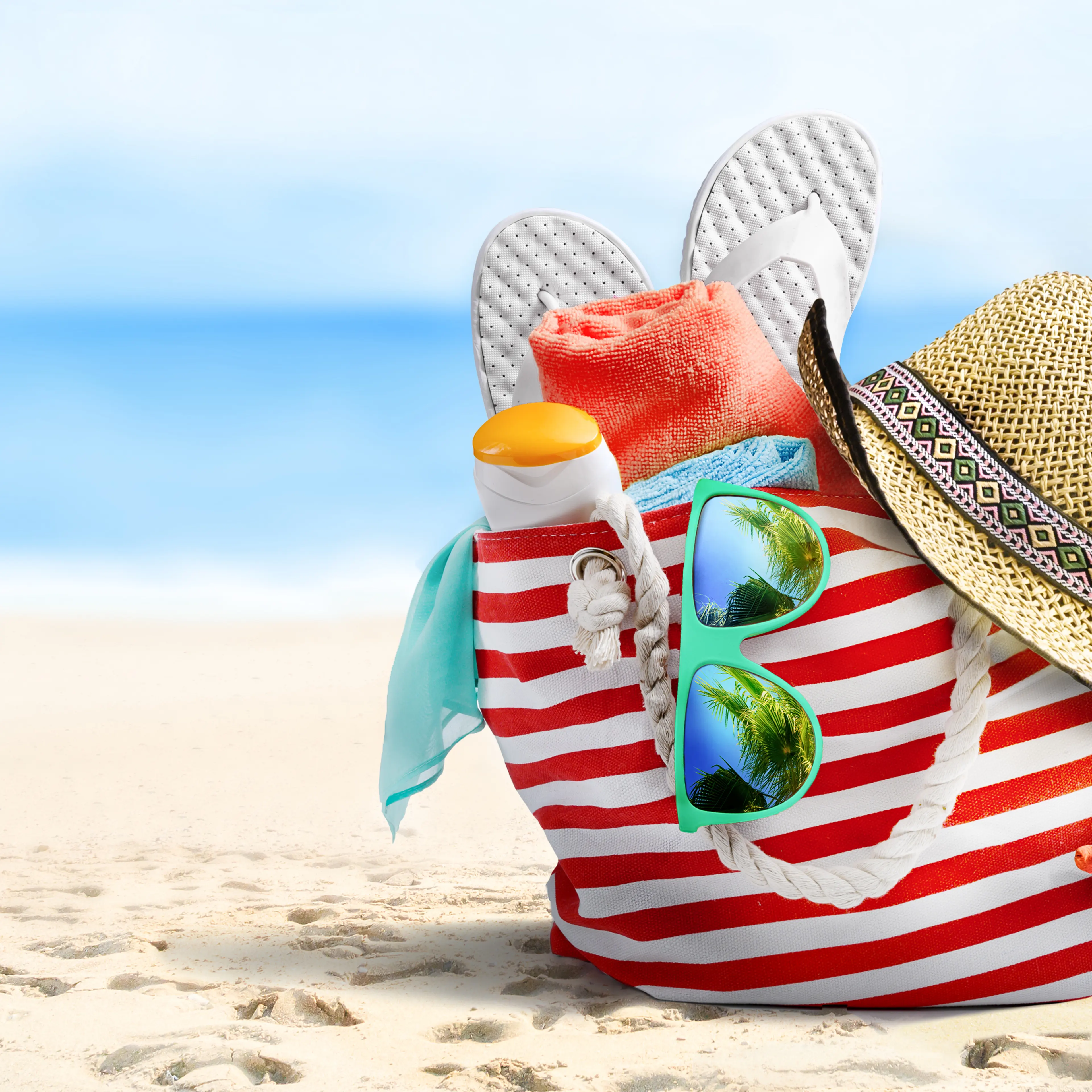 Summer beach bag and accessories on sandy beach and sea.