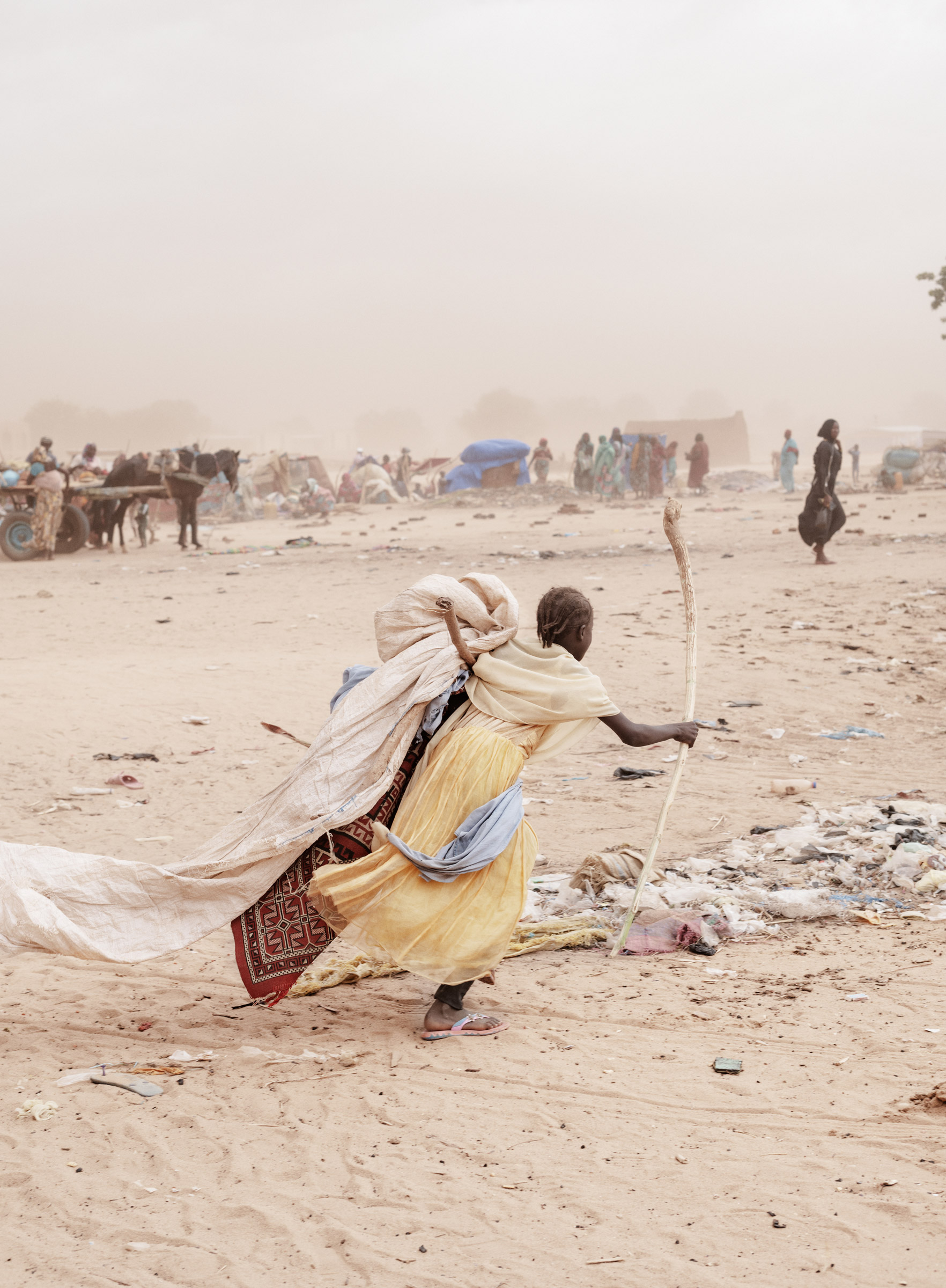 A girl runs carrying her belongings in search of a shelter to hide from the sandstorm and the looming rain in Adré refugee camp.