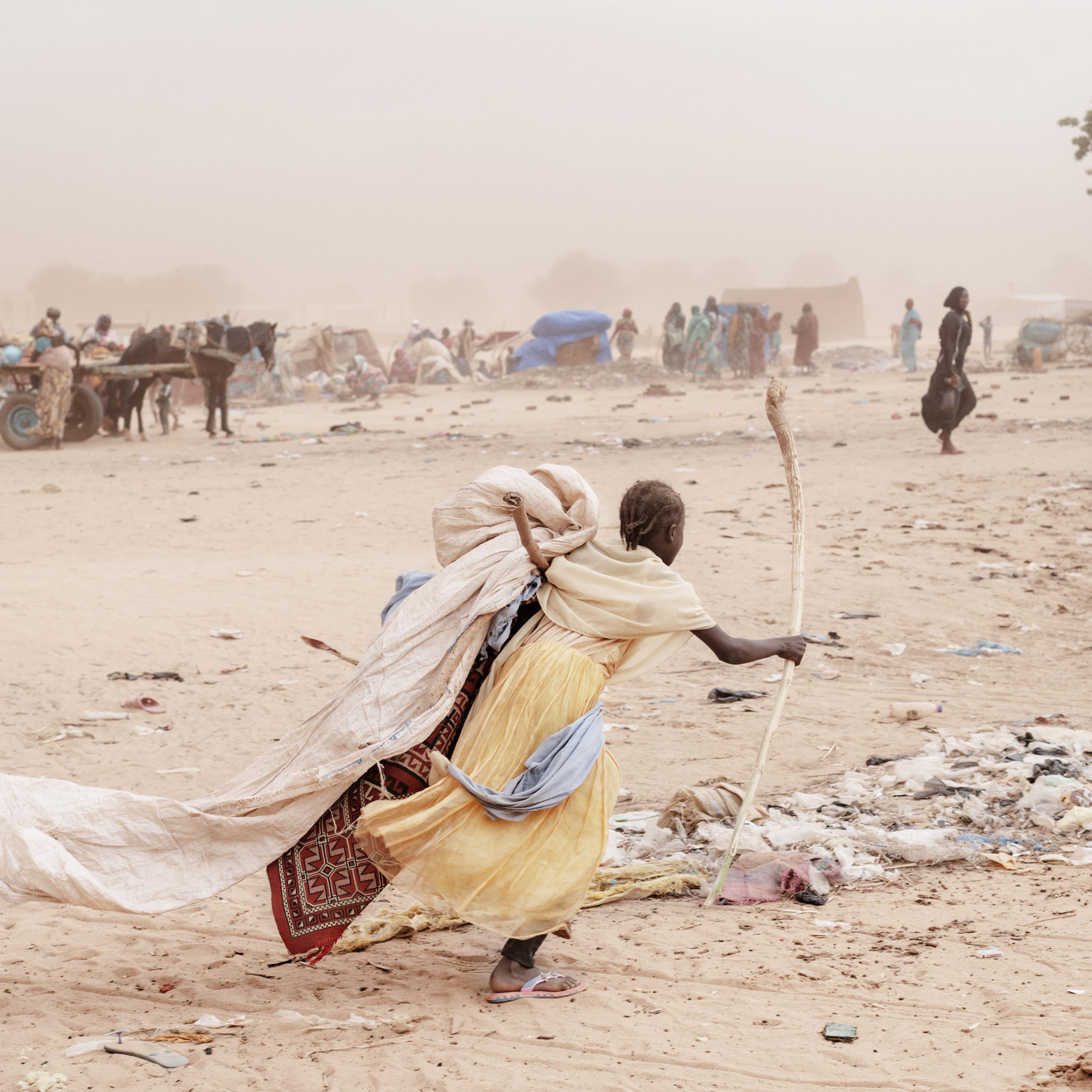 A girl runs carrying her belongings in search of a shelter to hide from the sandstorm and the looming rain in Adré refugee camp.