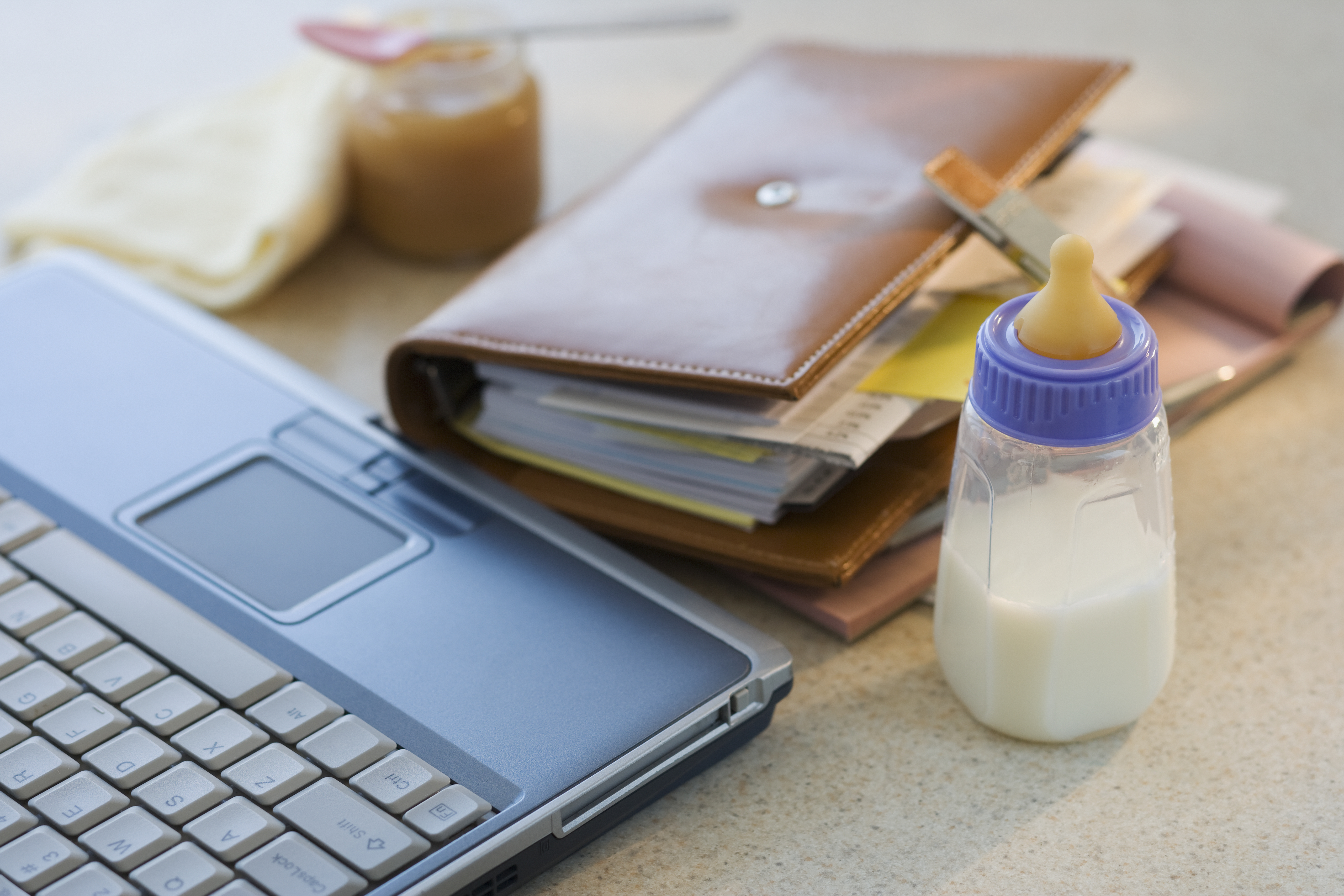 Laptop, planner and baby bottle on table