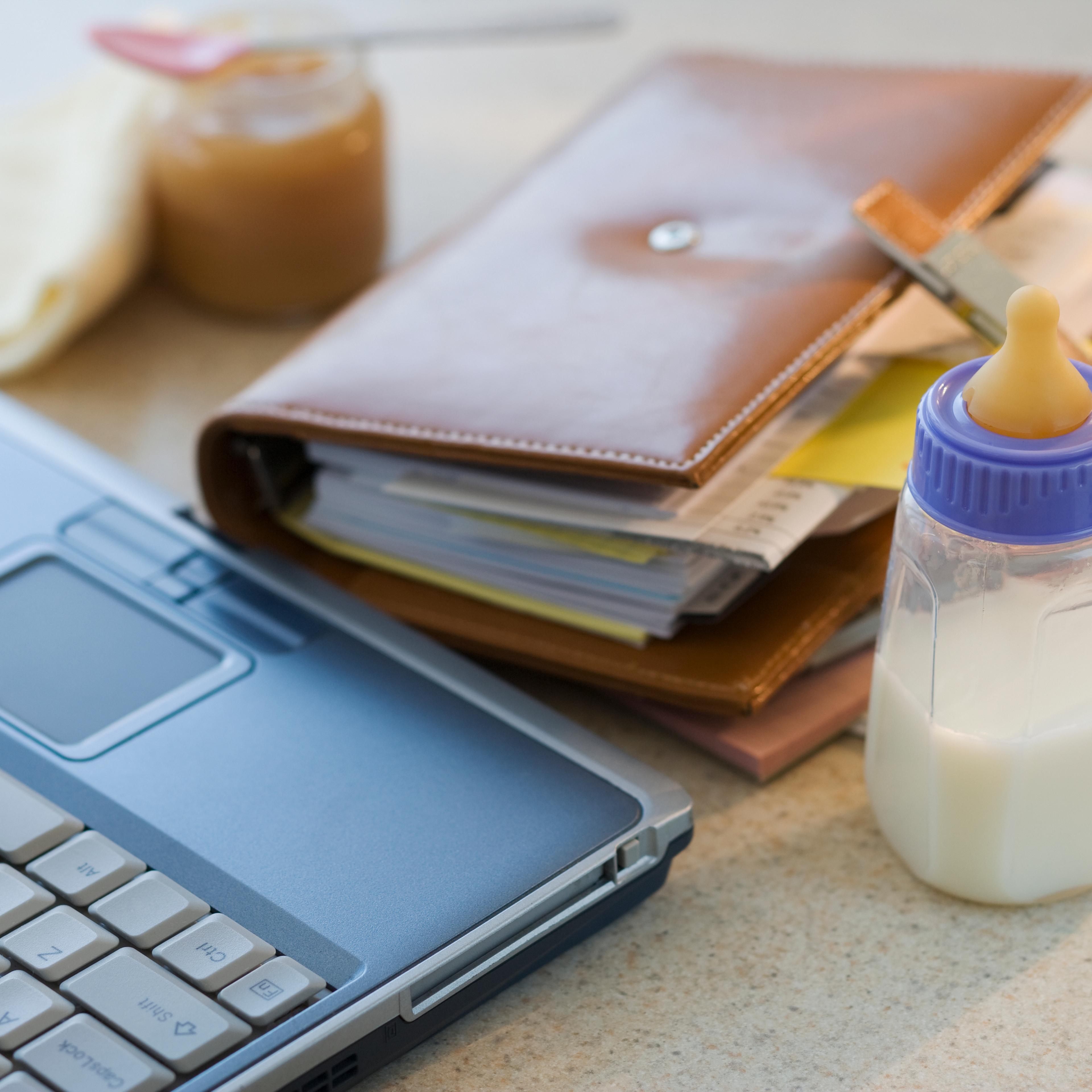 Laptop, planner and baby bottle on table