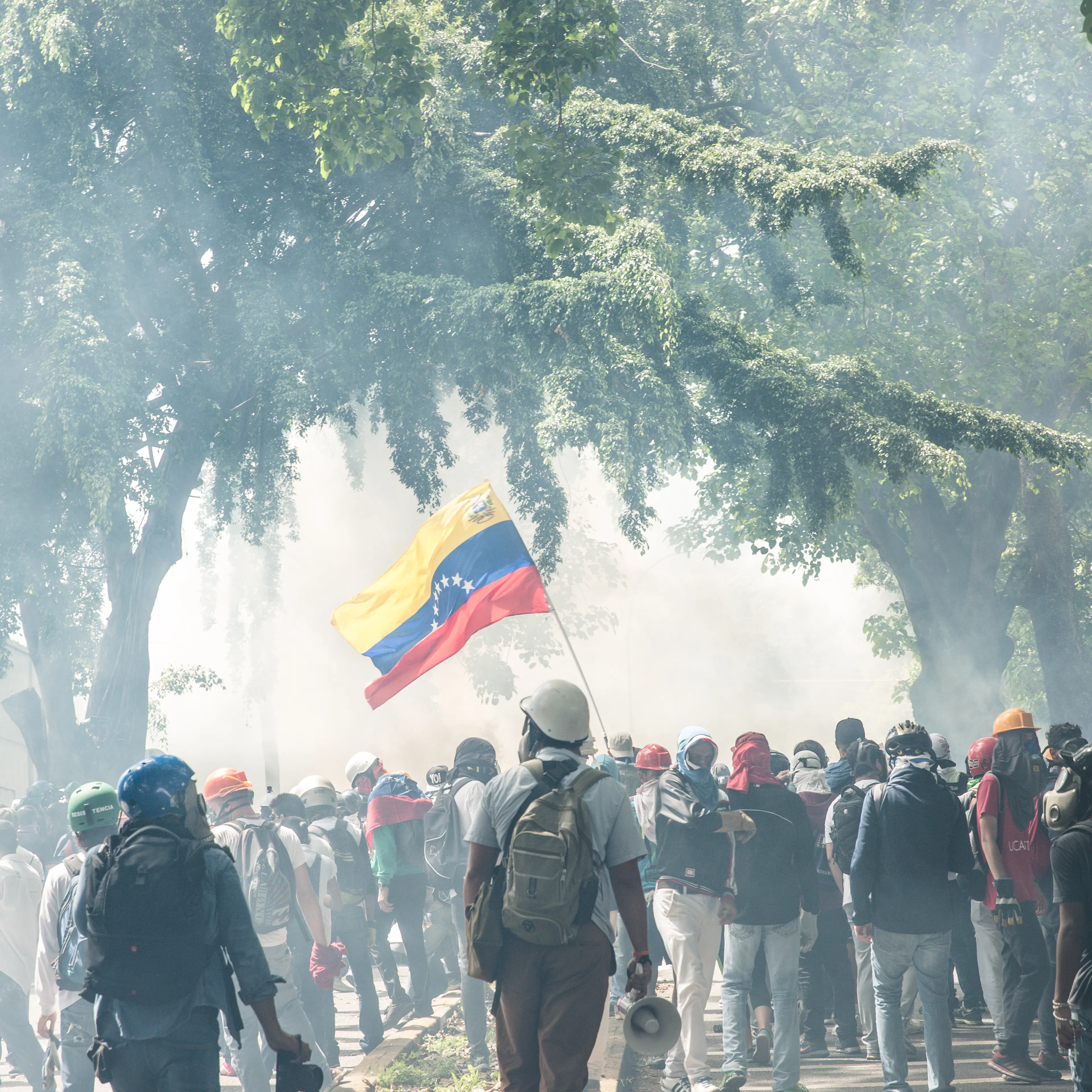 A group of protesters hold a Venezuelan flag as the air is thick with tear gas.