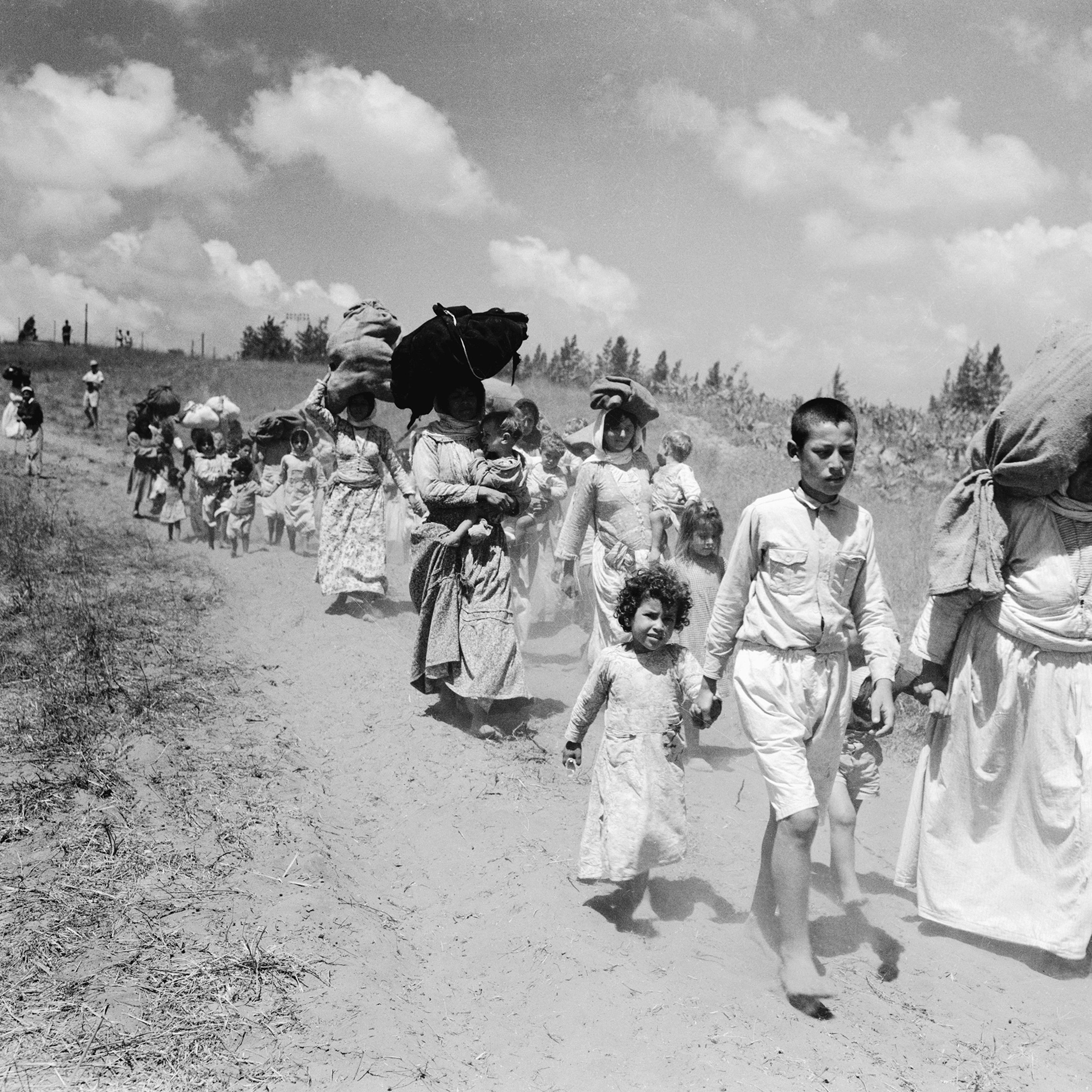 Arab refugees, mostly women and children, from village near Haifa begin a three mile hike carrying large bundles of personal possessions to the Arab lines in Tulkarim, West Bank, on June 26, 1948.